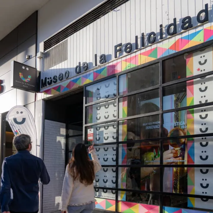 De buitenkant van Museo de la Felicidad met een kleurrijke gevel, een groot uithangbord en mensen die het gebouw binnengaan