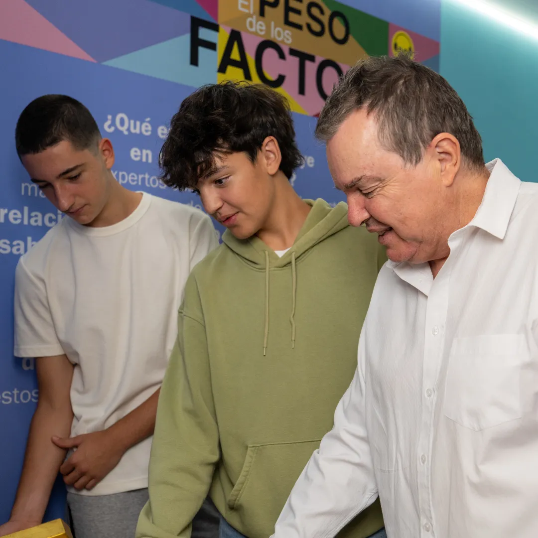 Three people interacting with an exhibit in front of a colorful wall with text