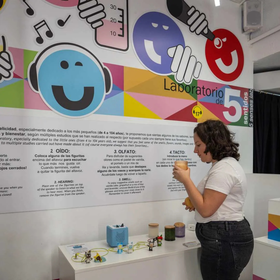 Een vrouw bekijkt een interactieve tentoonstelling met kleurrijke afbeeldingen en tekst op een muur in het Museo de la Felicidad.