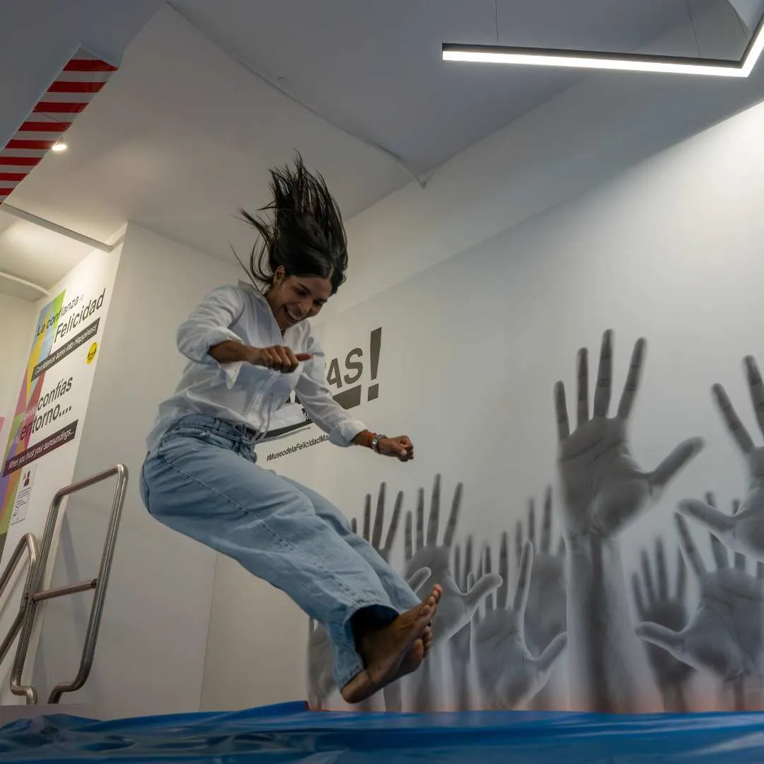 Een vrouw die op een blauwe trampoline springt in een binnenruimte met handafdrukken en tekst op de muur