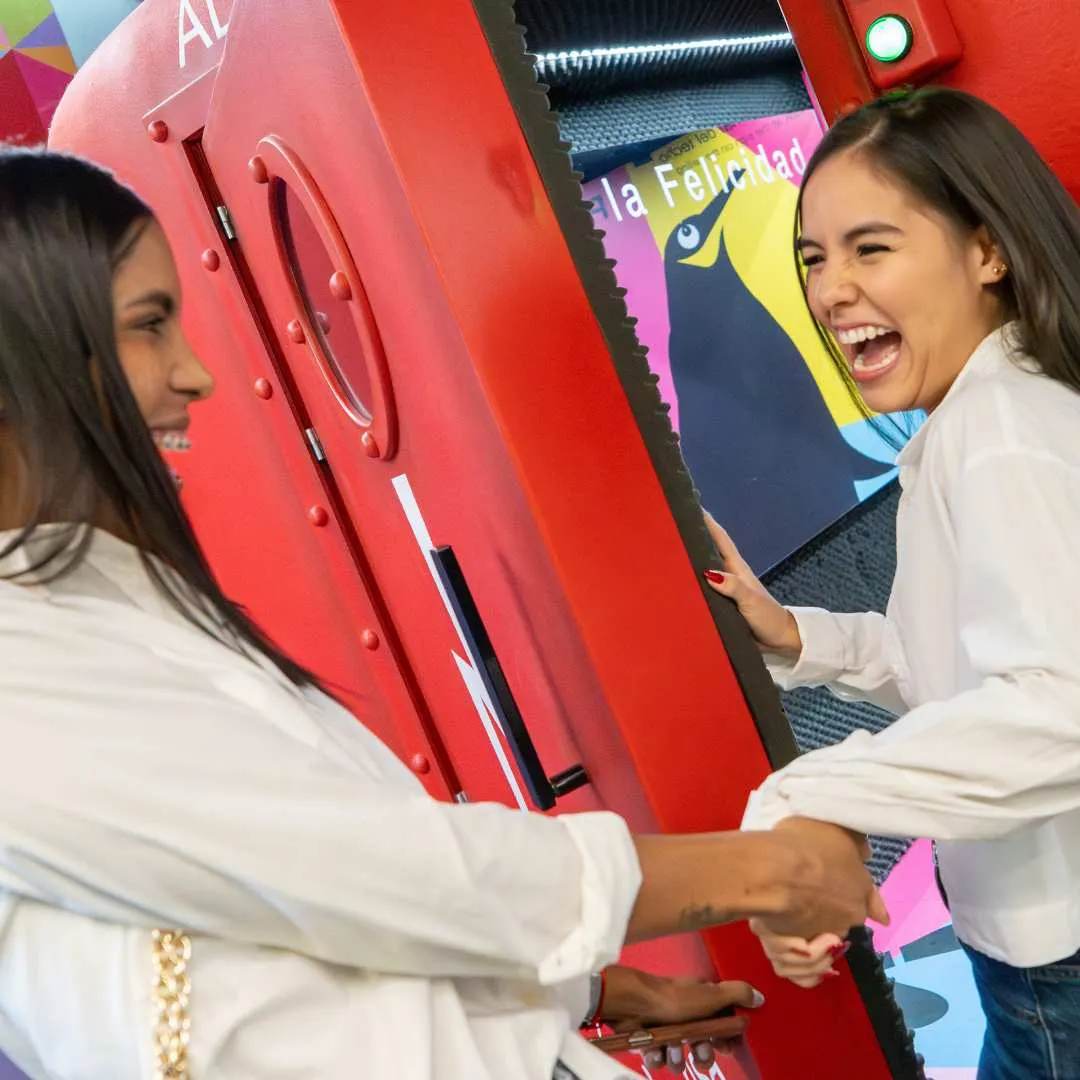 Twee vrouwen die lachen en interageren met een rode interactieve tentoonstelling in Museo de la Felicidad
