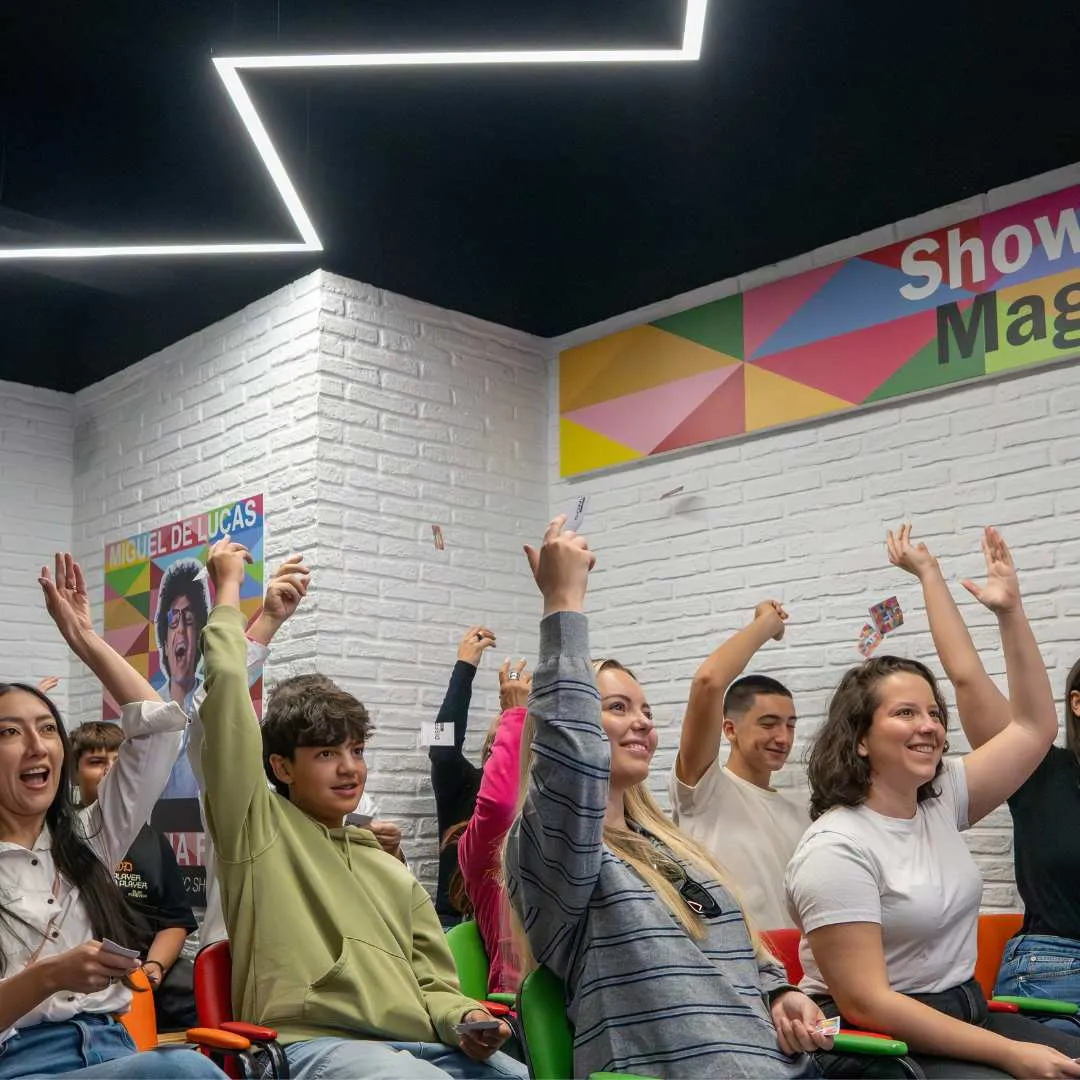 Groep mensen die handen opsteken in een interactieve tentoonstellingsruimte met kleurrijke muurkunst en witte bakstenen muren