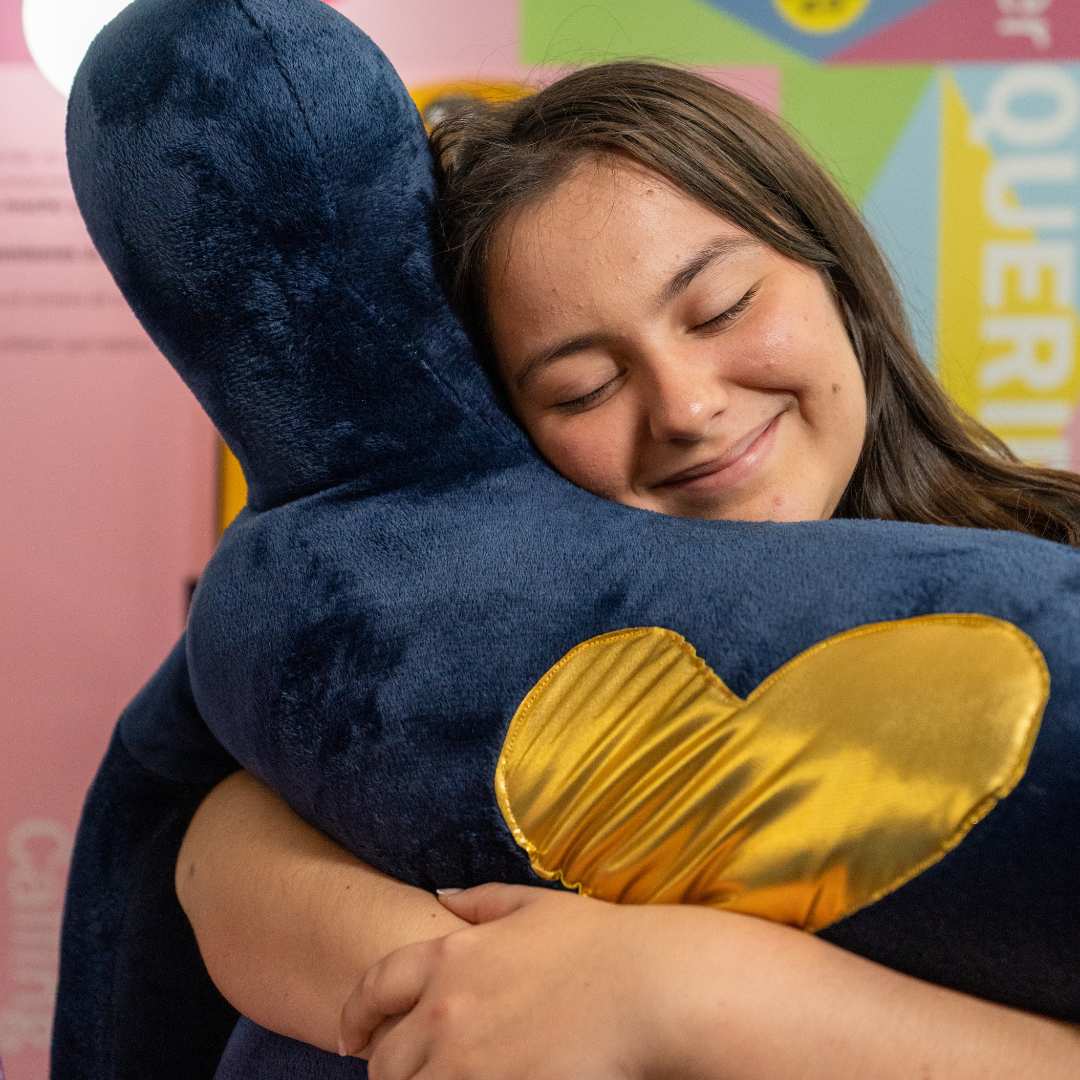 Een vrouw die een grote blauwe pluche figuur met een gouden hart omhelst