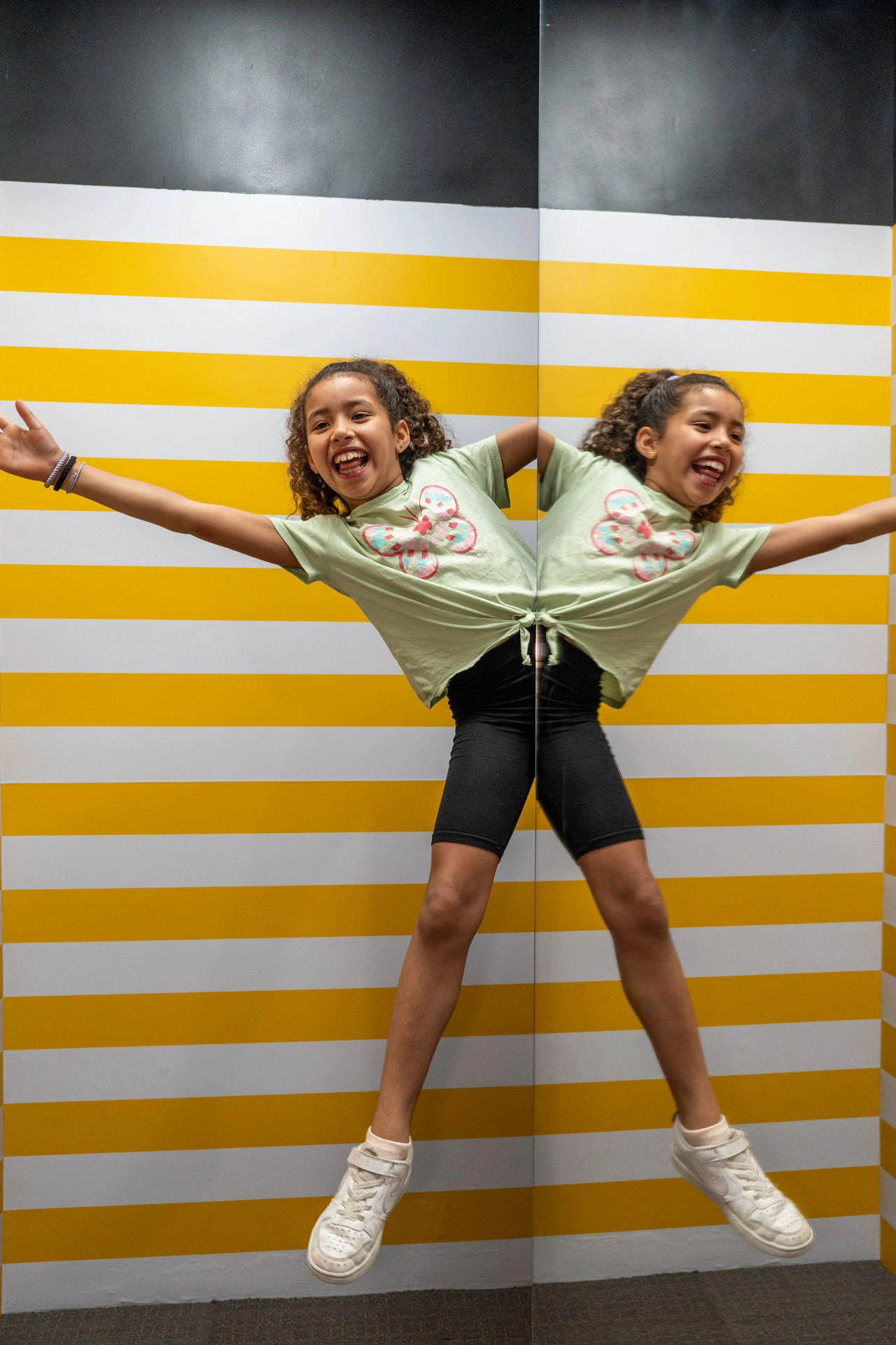 Girl appearing split in half by yellow and white striped optical illusion wall at Museum of Illusions
