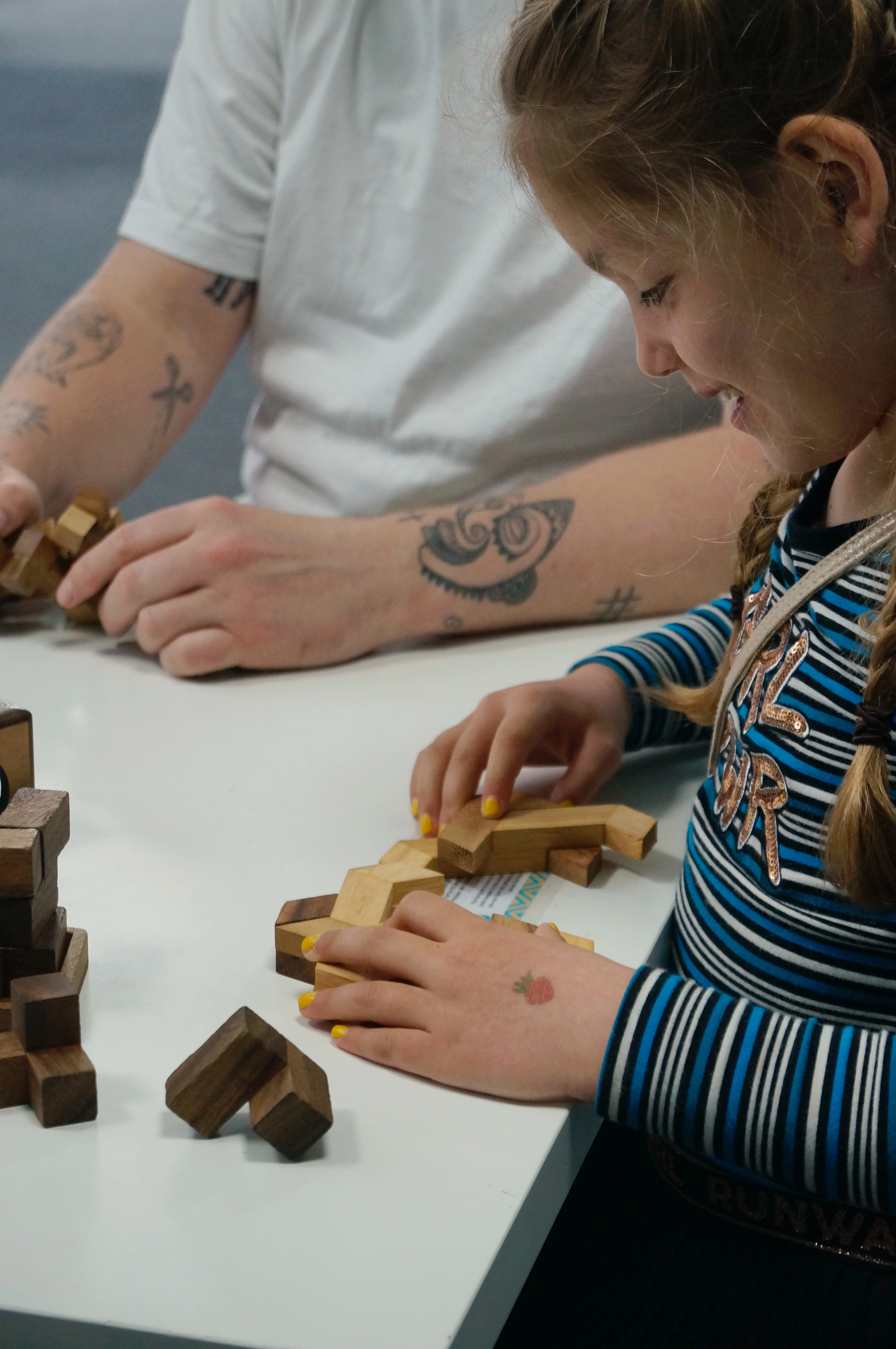 Girl and adult with tattooed arms assembling wooden block puzzles at a white table