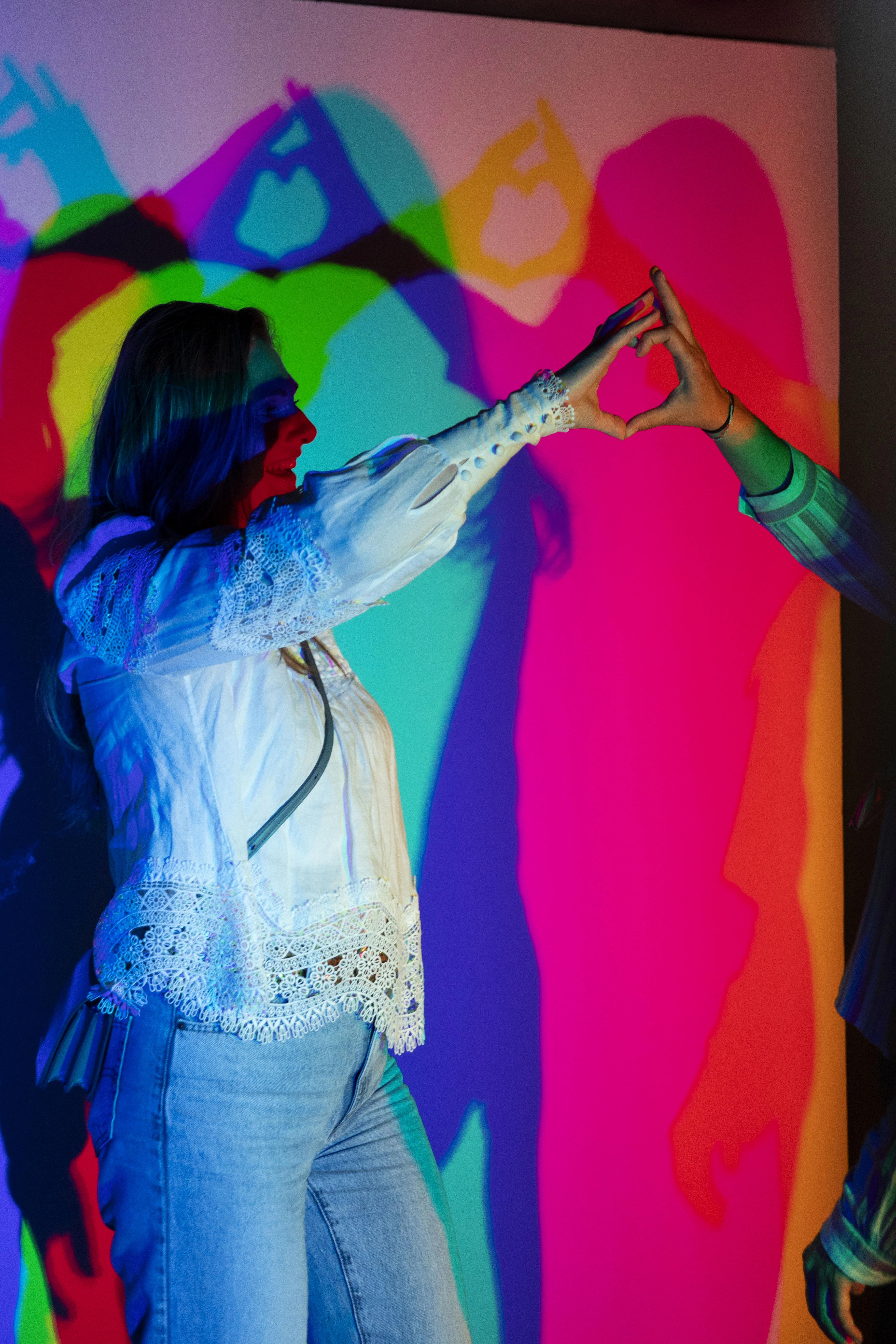 Two people creating hand gestures that form colorful shadow projections on a wall in an interactive optical illusion exhibit