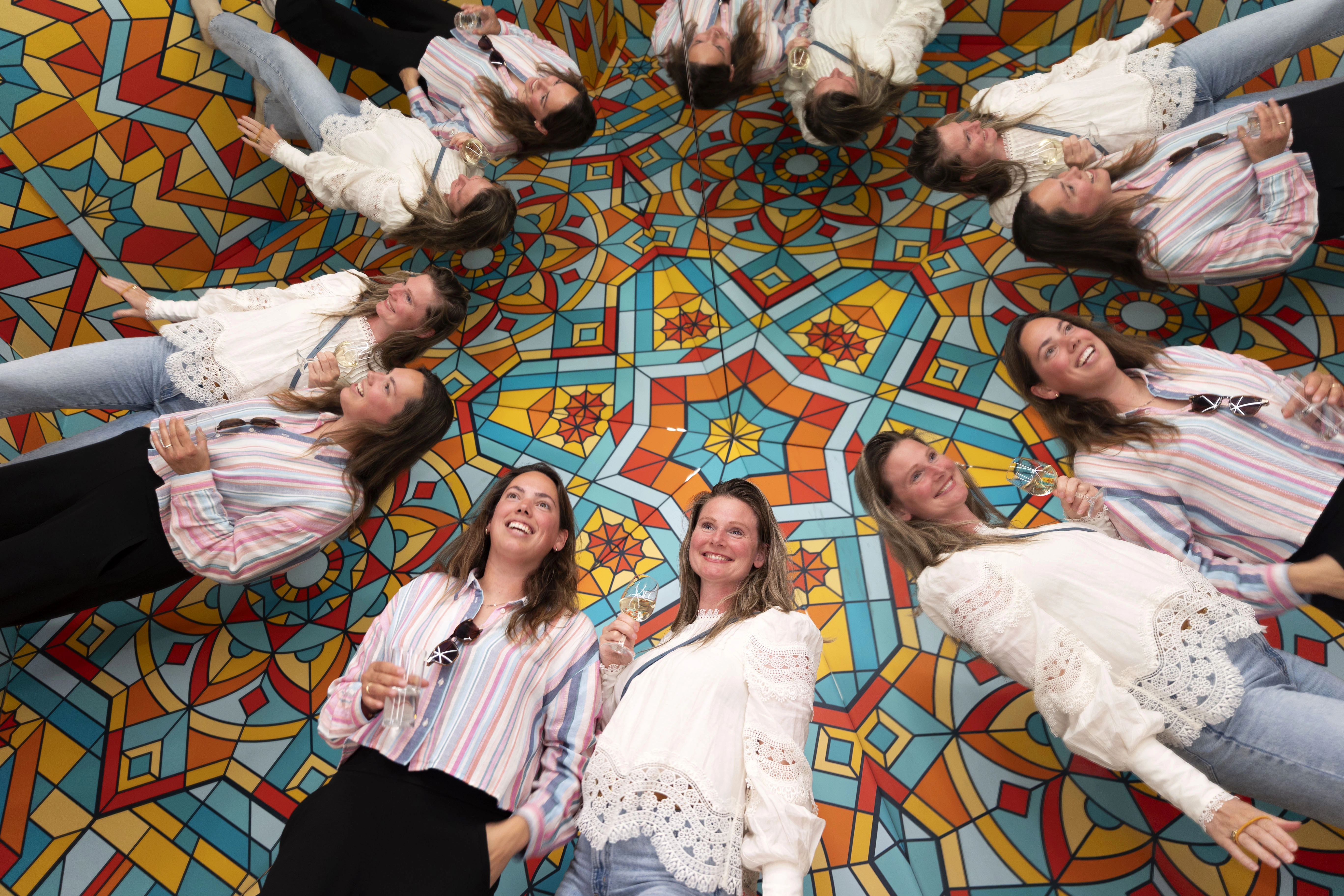 Group of people interacting with a colorful geometric optical illusion floor exhibit
