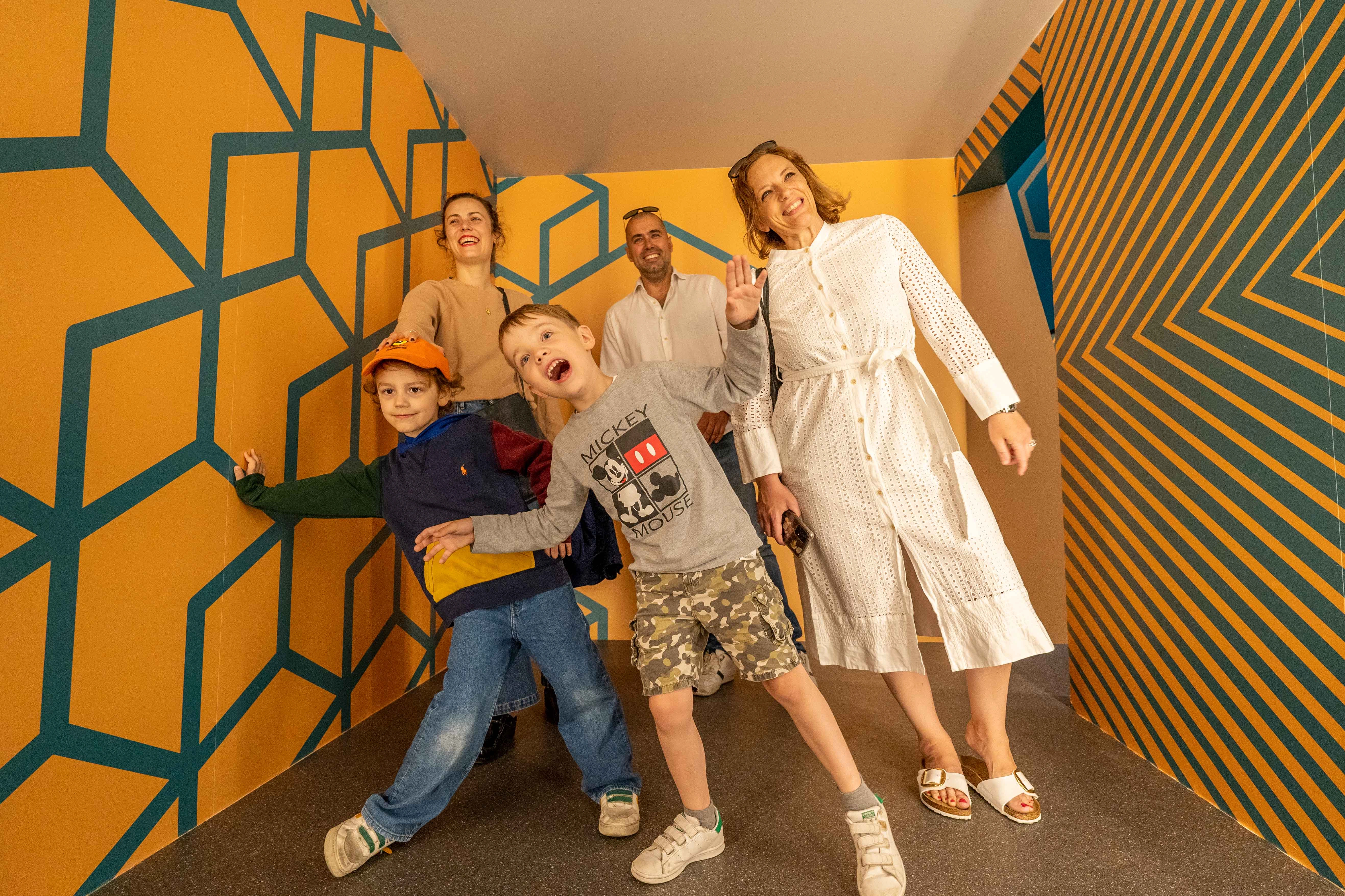 Group of people interacting with colorful geometric optical illusion walls in a museum exhibit space with distorted perspective