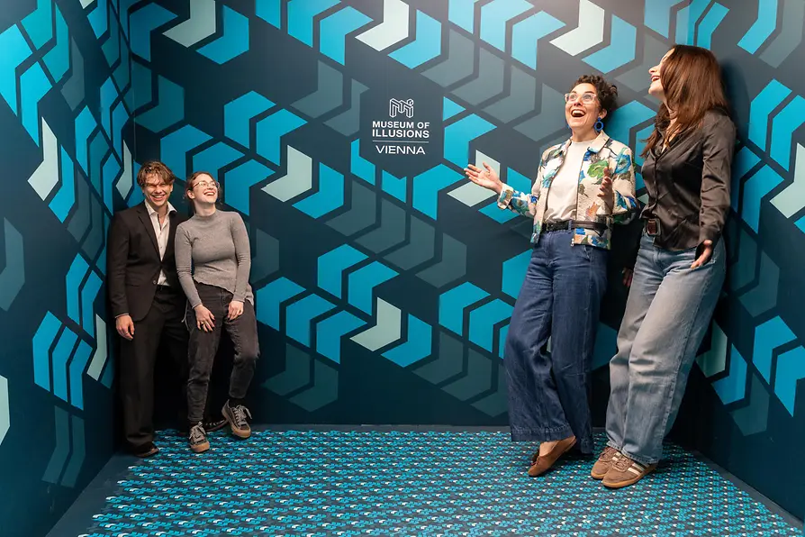 Drie mensen in een kamer met blauwe geometrische patronen op de muren en vloer, die een optische illusie ervaren in het Museum van Illusies Wenen