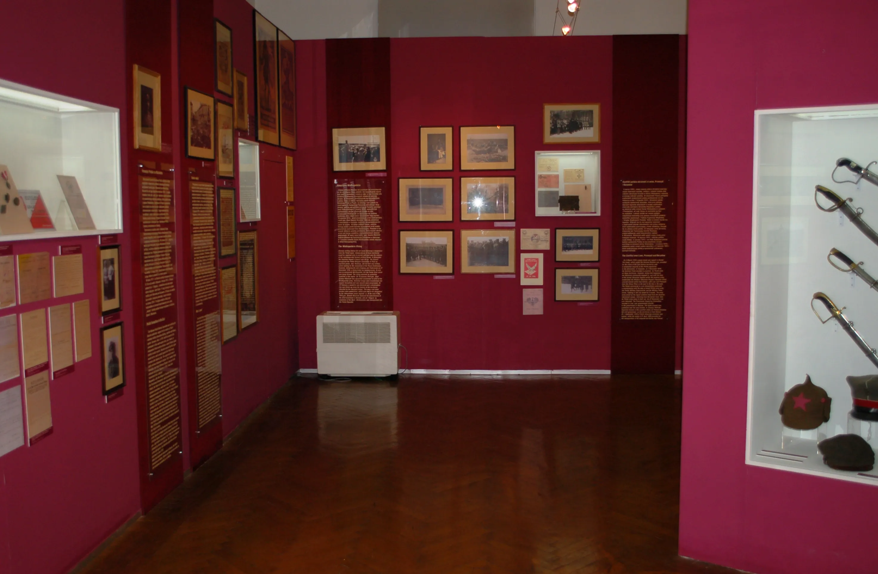 Interior gallery with red walls displaying framed documents and artifacts in glass cases