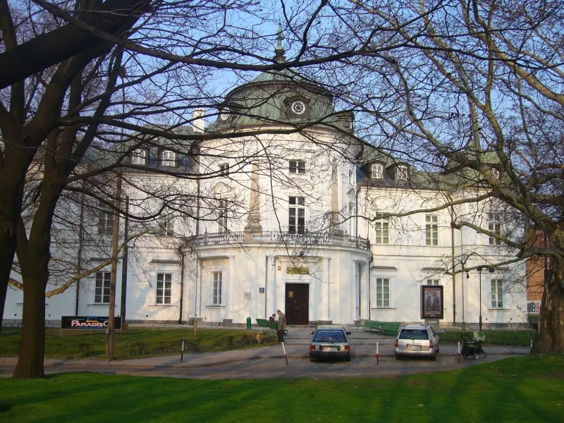 White neoclassical building with a central dome and columns, surrounded by bare trees and a green lawn
