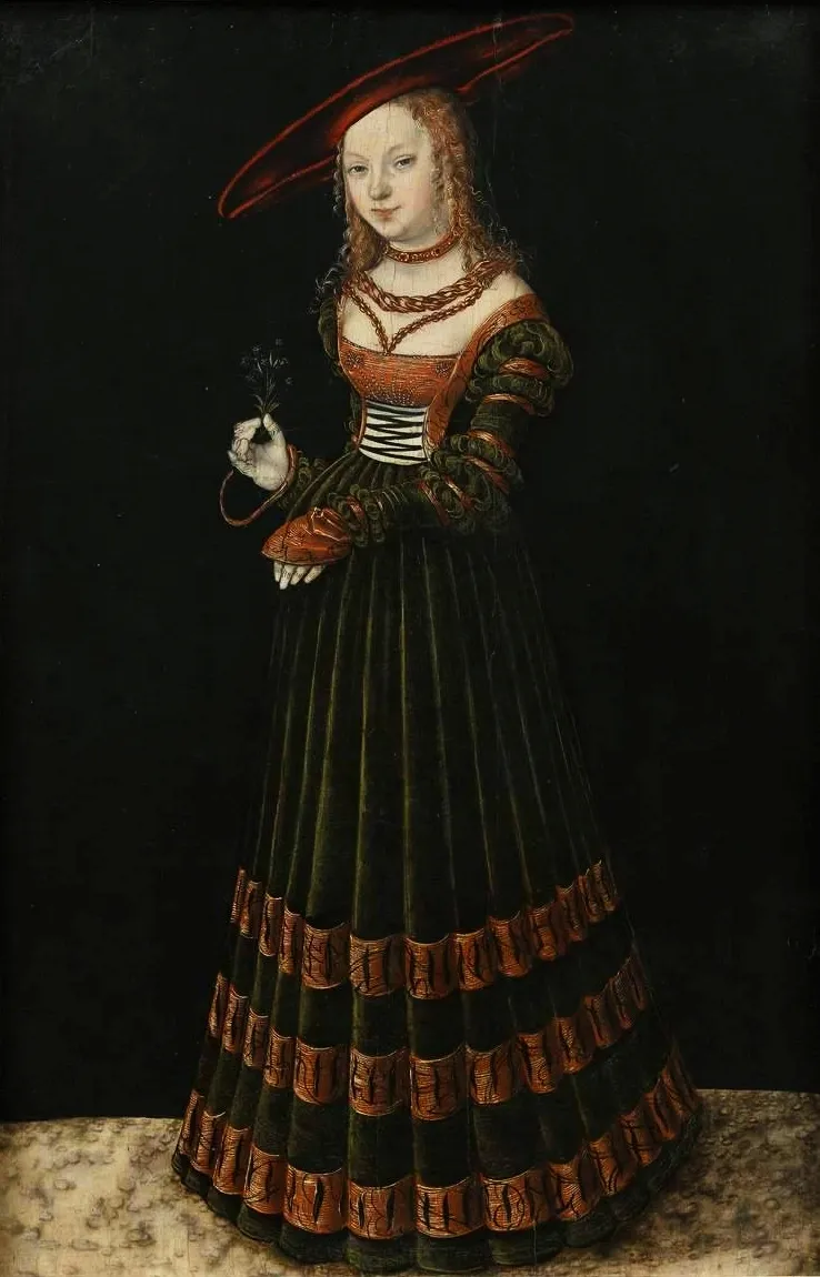 Una mujer con un vestido renacentista verde oscuro y rojo con un sombrero de ala ancha, que sostiene un ramillete de flores