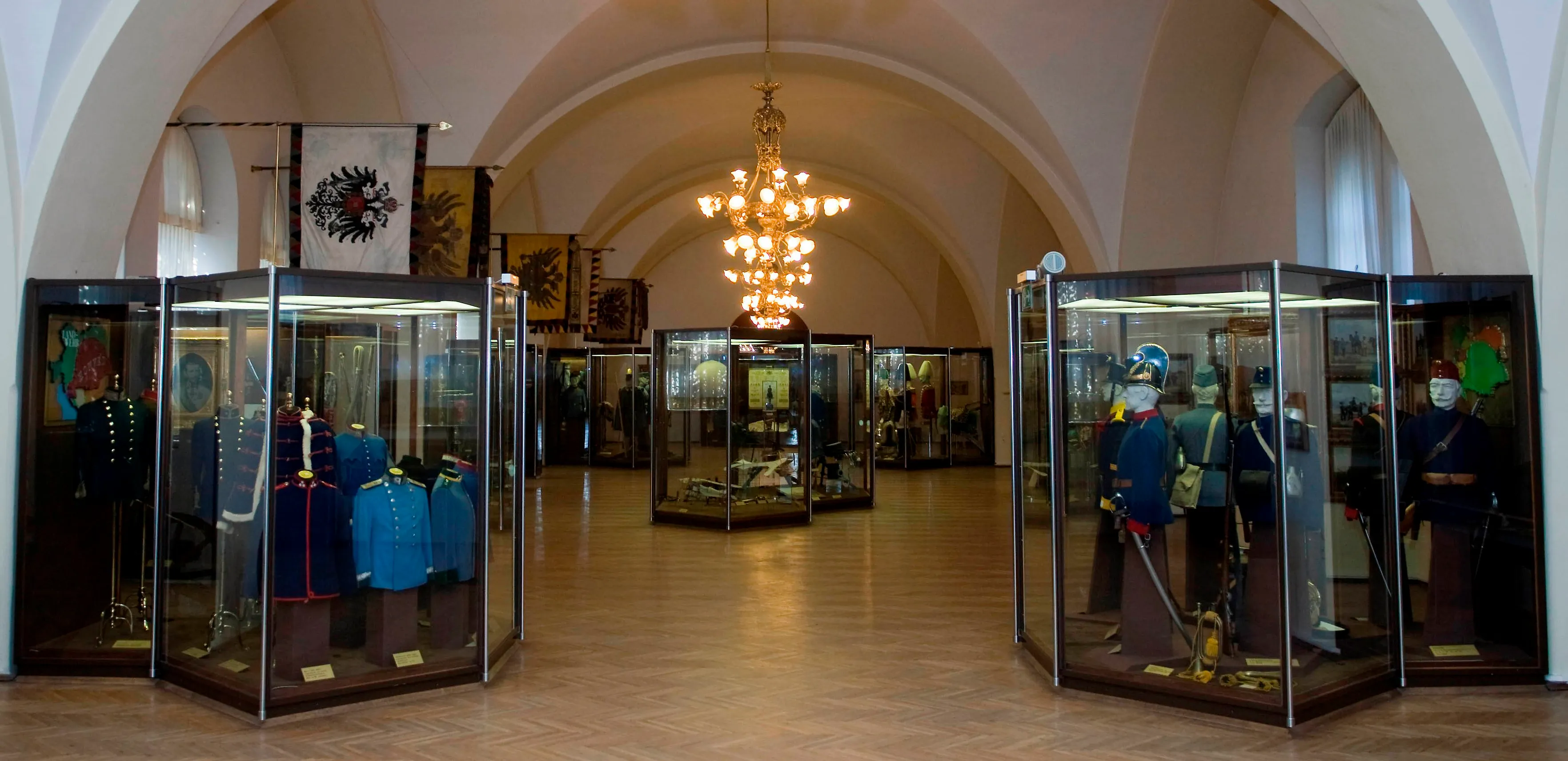 Binnenhal met boogramen, een centrale kroonluchter en vitrines met militaire uniformen en artefacten.