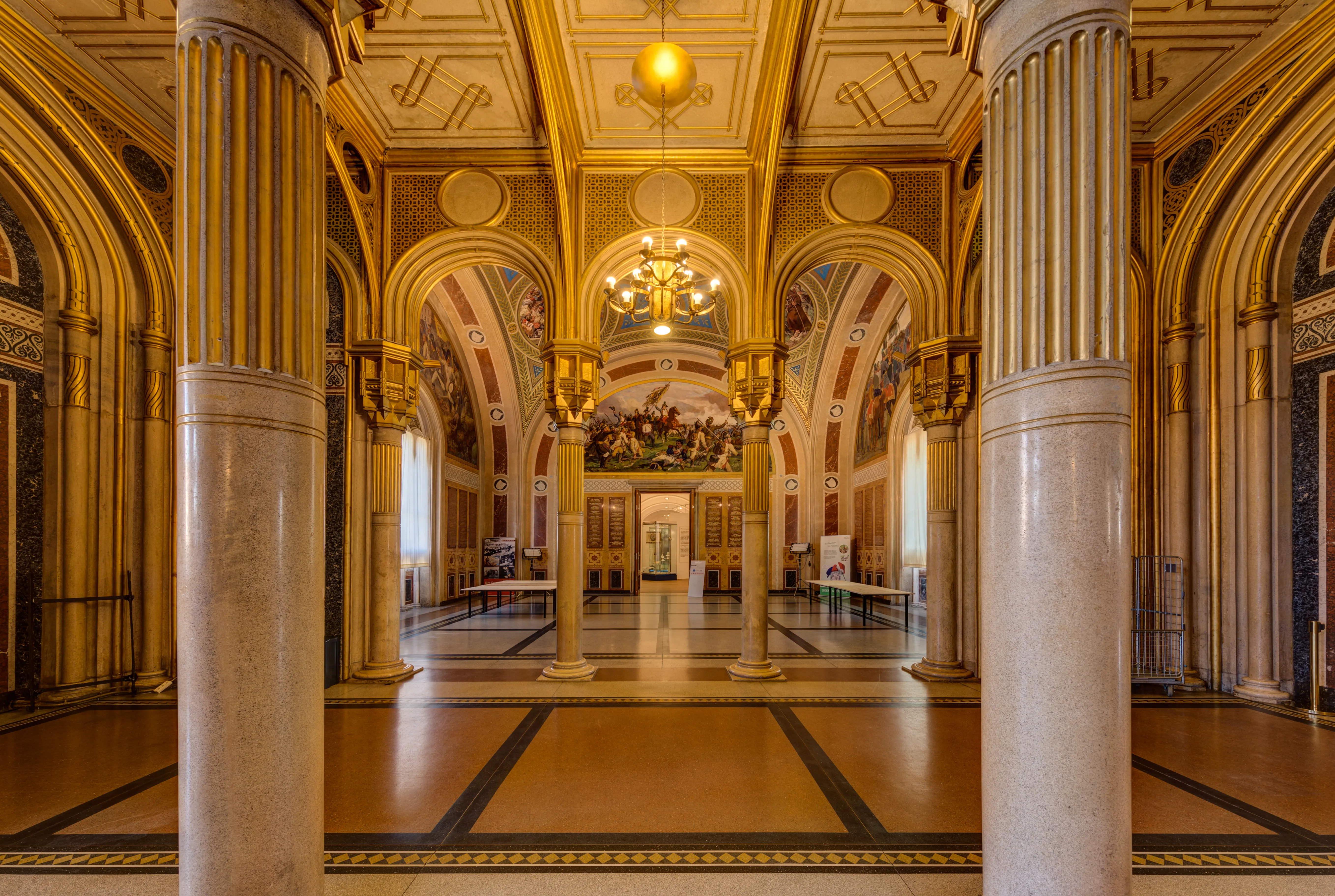 Grote zaal met sierlijke gouden zuilen, gewelfde plafonds en een kroonluchter