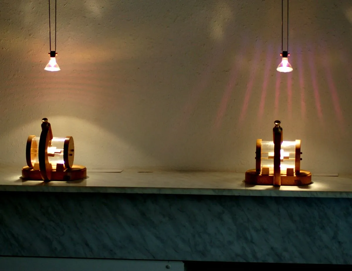 Dos vitrinas iluminadas en miniatura con pequeñas figuras en su interior, dispuestas sobre una superficie de mármol bajo luces colgantes.
