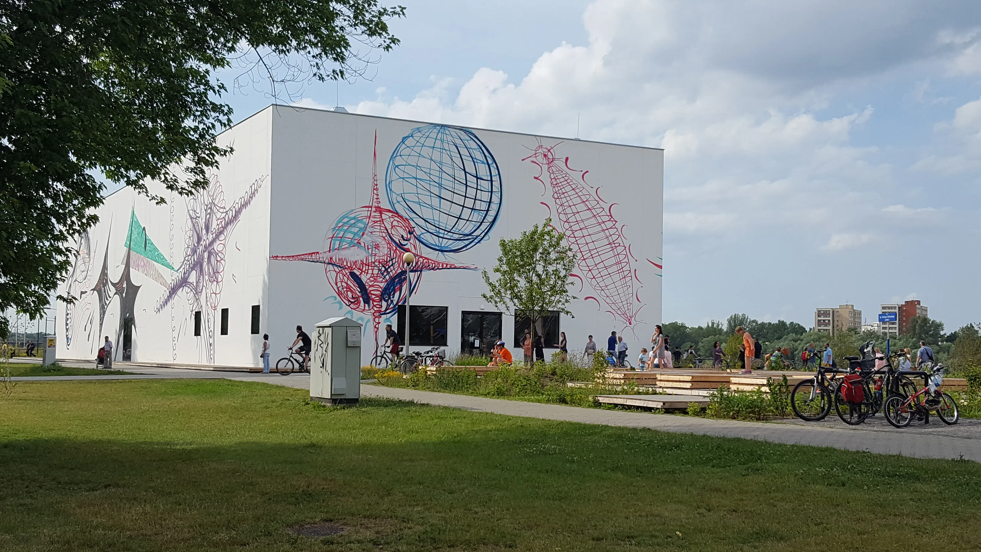 White building with abstract art murals on its facade, surrounded by green grass and trees