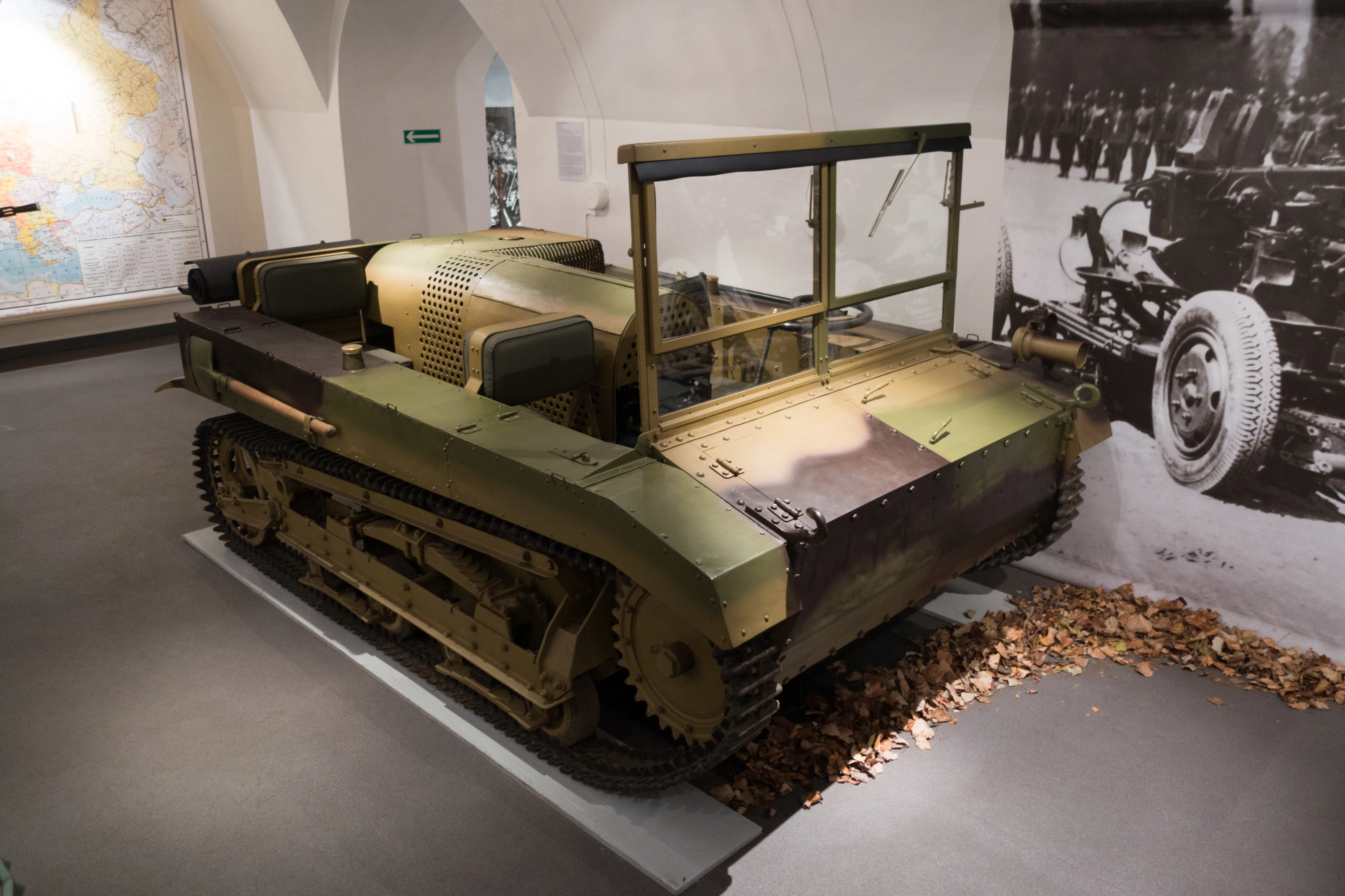 Een groen militair rupsvoertuig binnenshuis tentoongesteld met een historische foto op de achtergrond