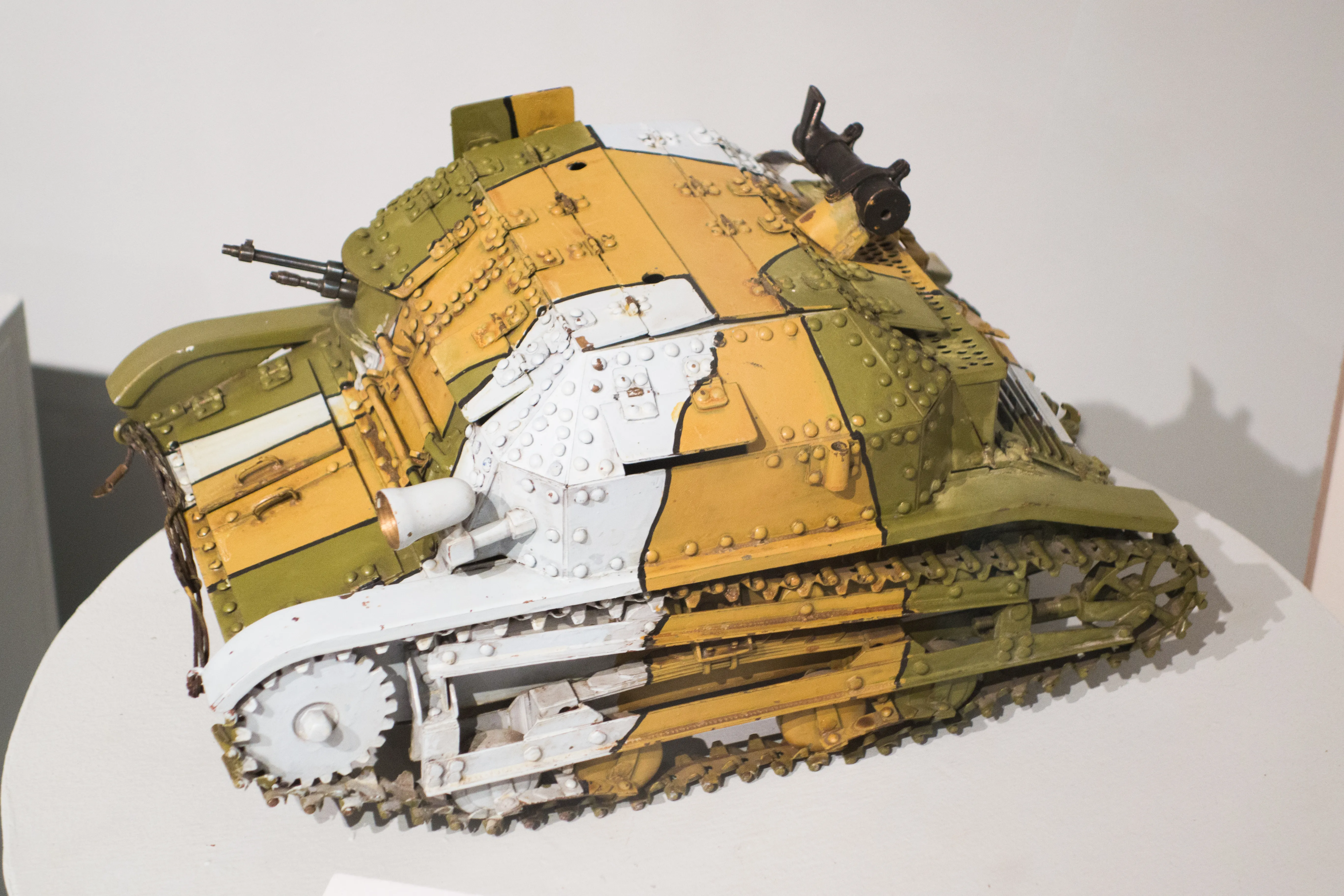 Een geel en groen militair tankmodel met witte markeringen op een wit voetstuk