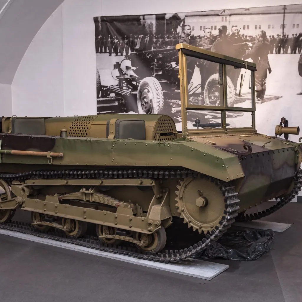Een groen militair rupsvoertuig tentoongesteld in een museumgalerij met een historische foto erachter