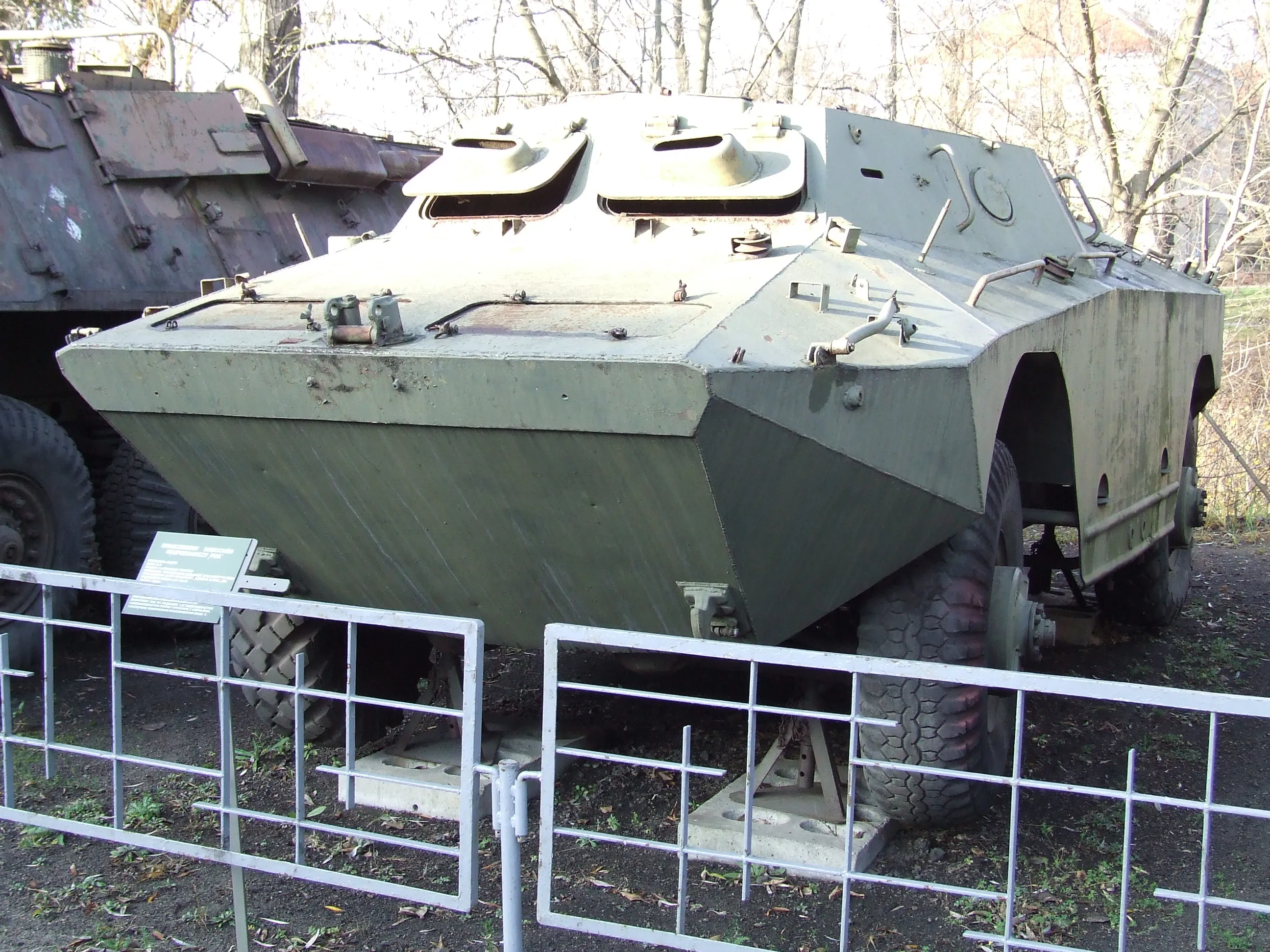 Un vehículo blindado de personal verde detrás de una valla de metal en un museo militar al aire libre