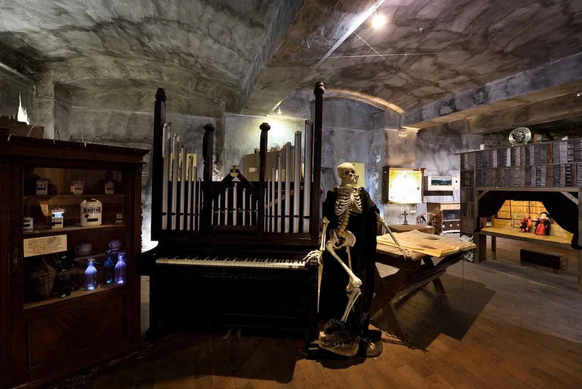 skeletfiguur die naast een piano staat in een schemerige kamer met stenen muren