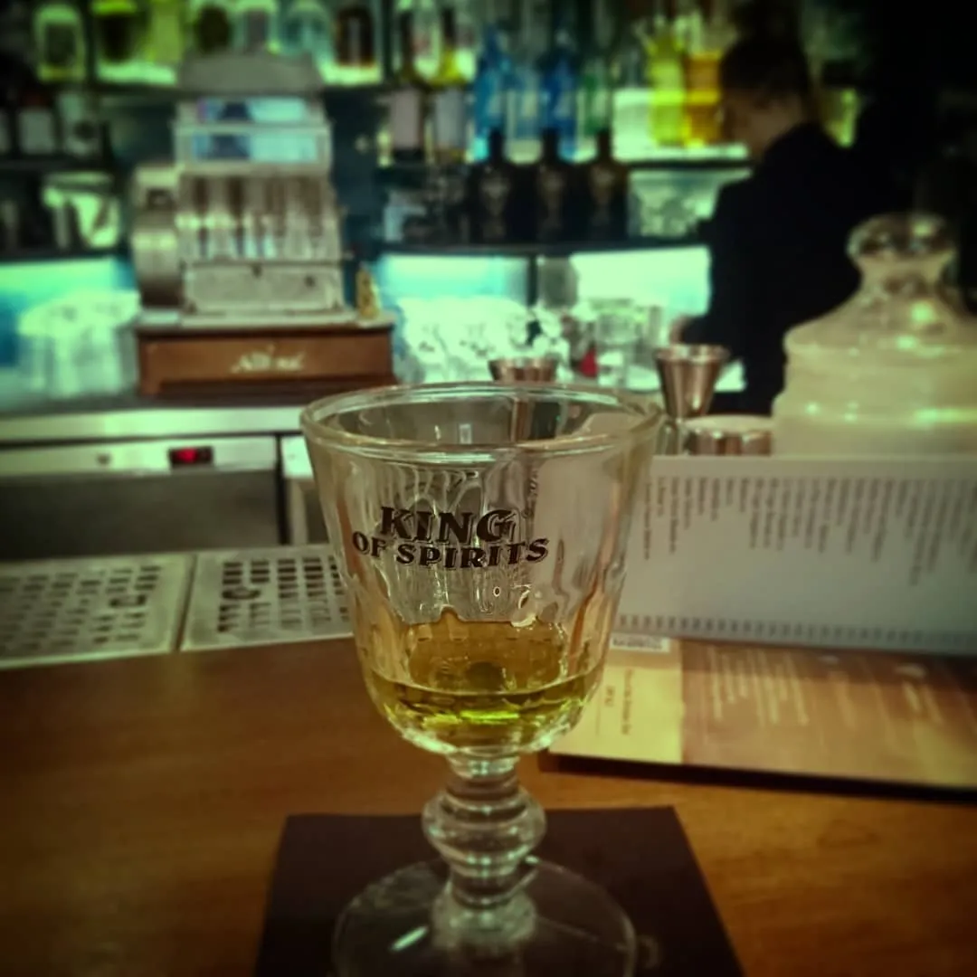 een glas absint op een bar met een menu en flessen op de achtergrond
