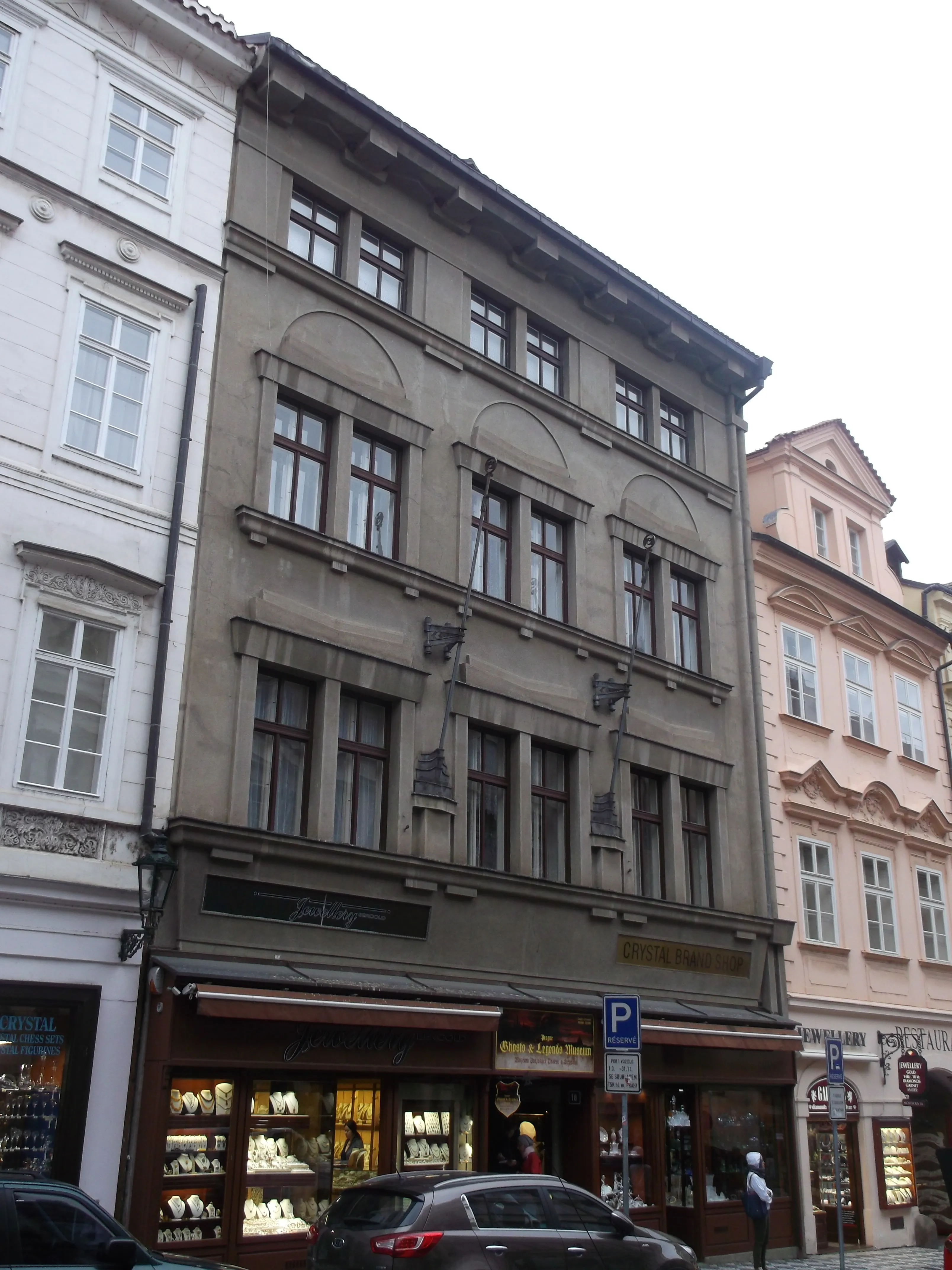 Een meerlaags gebouw met boogramen en een winkelpui op de begane grond, gelegen aan een straat in Praag.