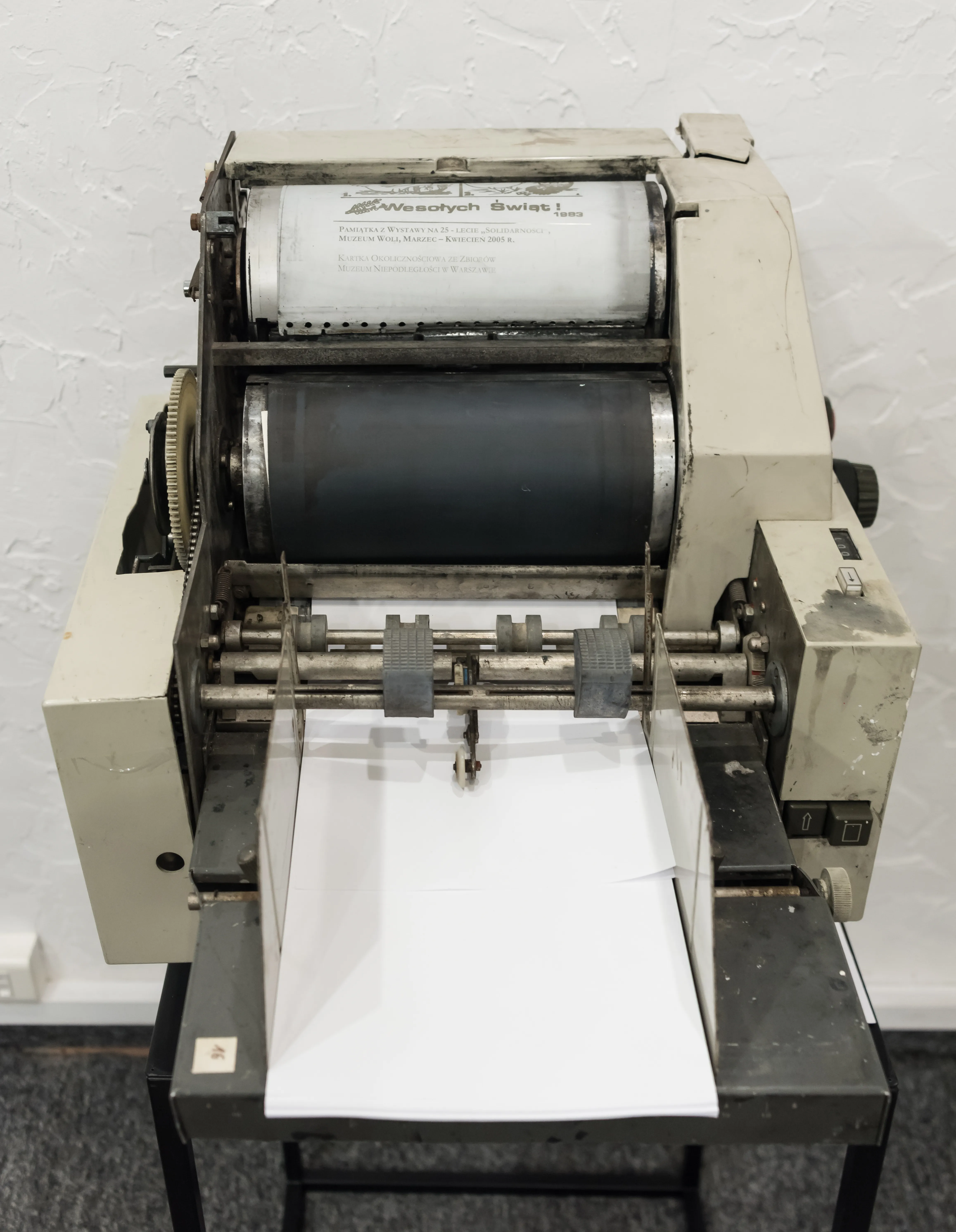 Een vintage drukpers met een rol papier en een bedrukt vel, tentoongesteld in een museum.