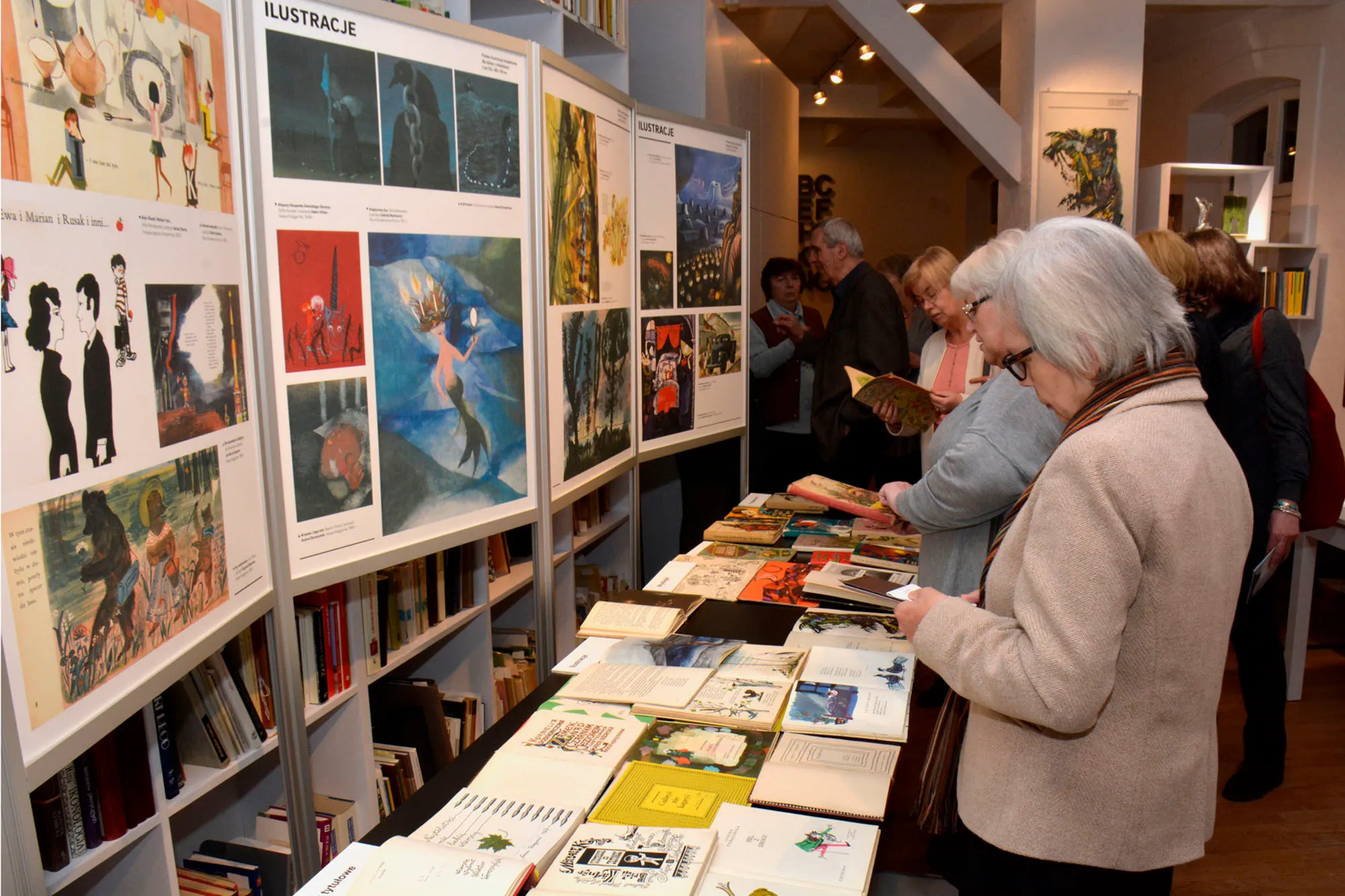 People viewing a display of illustrated books and posters on a wall in a museum gallery