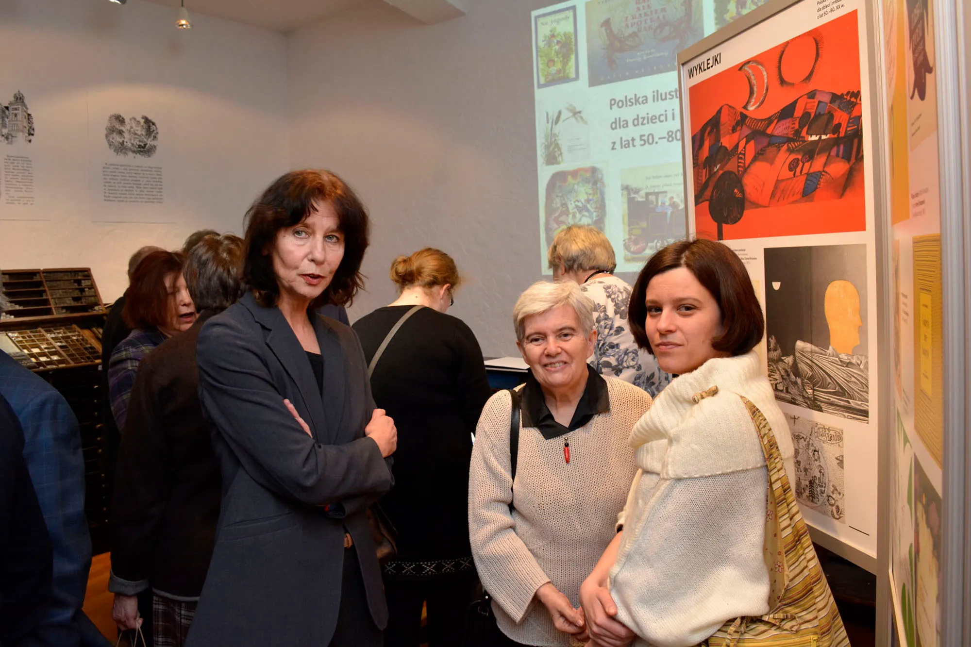 drie vrouwen die voor tentoonstellingspanelen met geïllustreerde posters en tekst staan in een museumgalerij