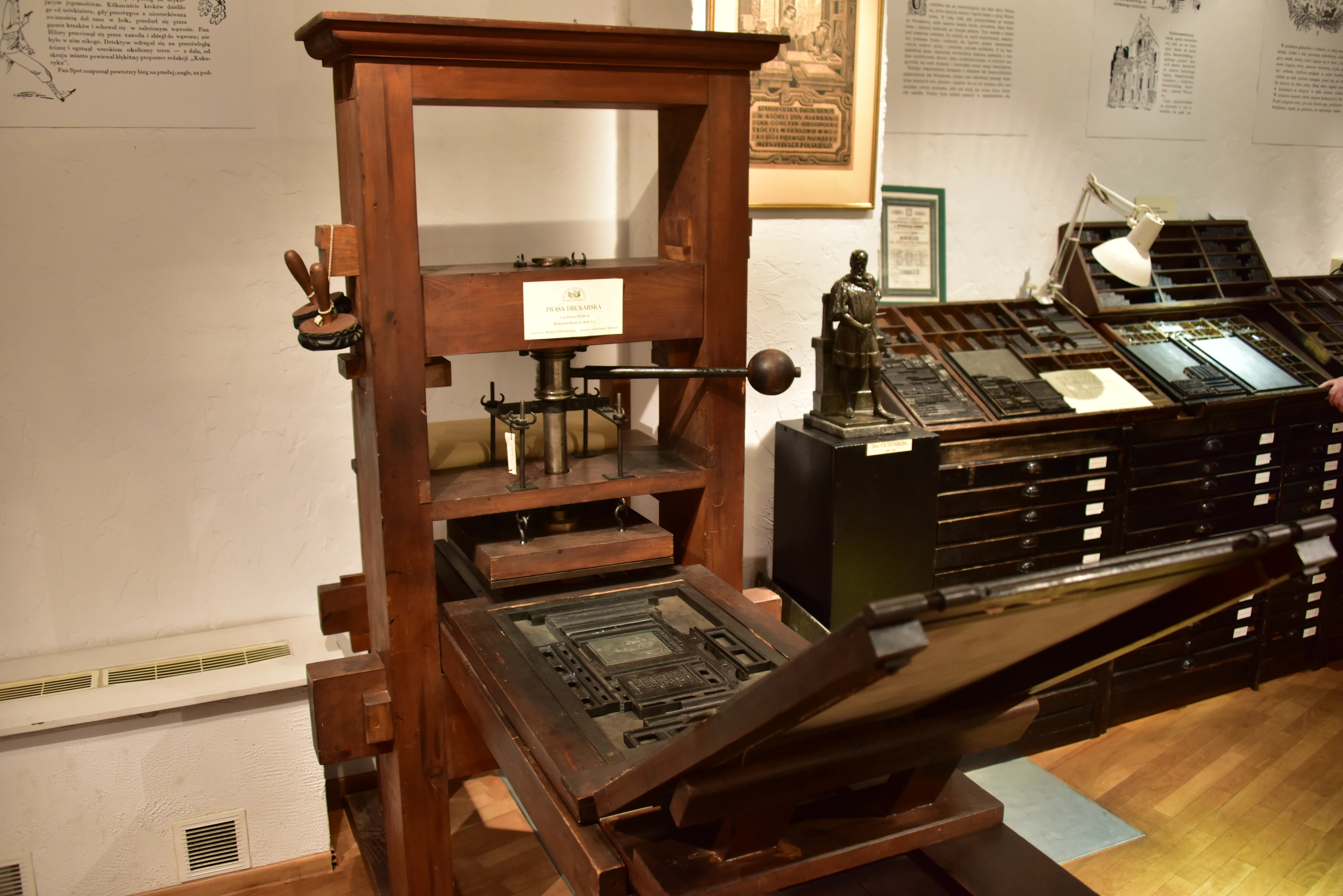 wooden printing press with metal components and a sign on the wall behind it