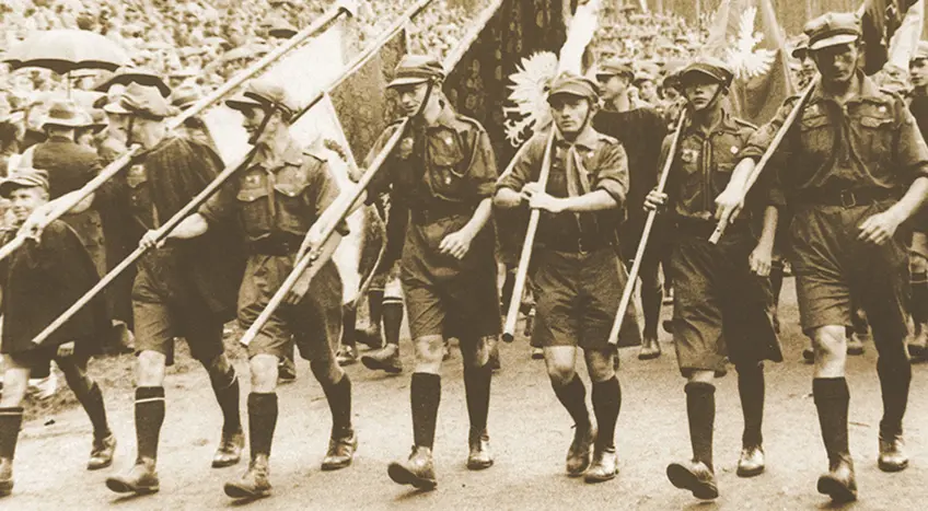 Groep scouts in vintage uniformen marcheren met vlaggen en geweren