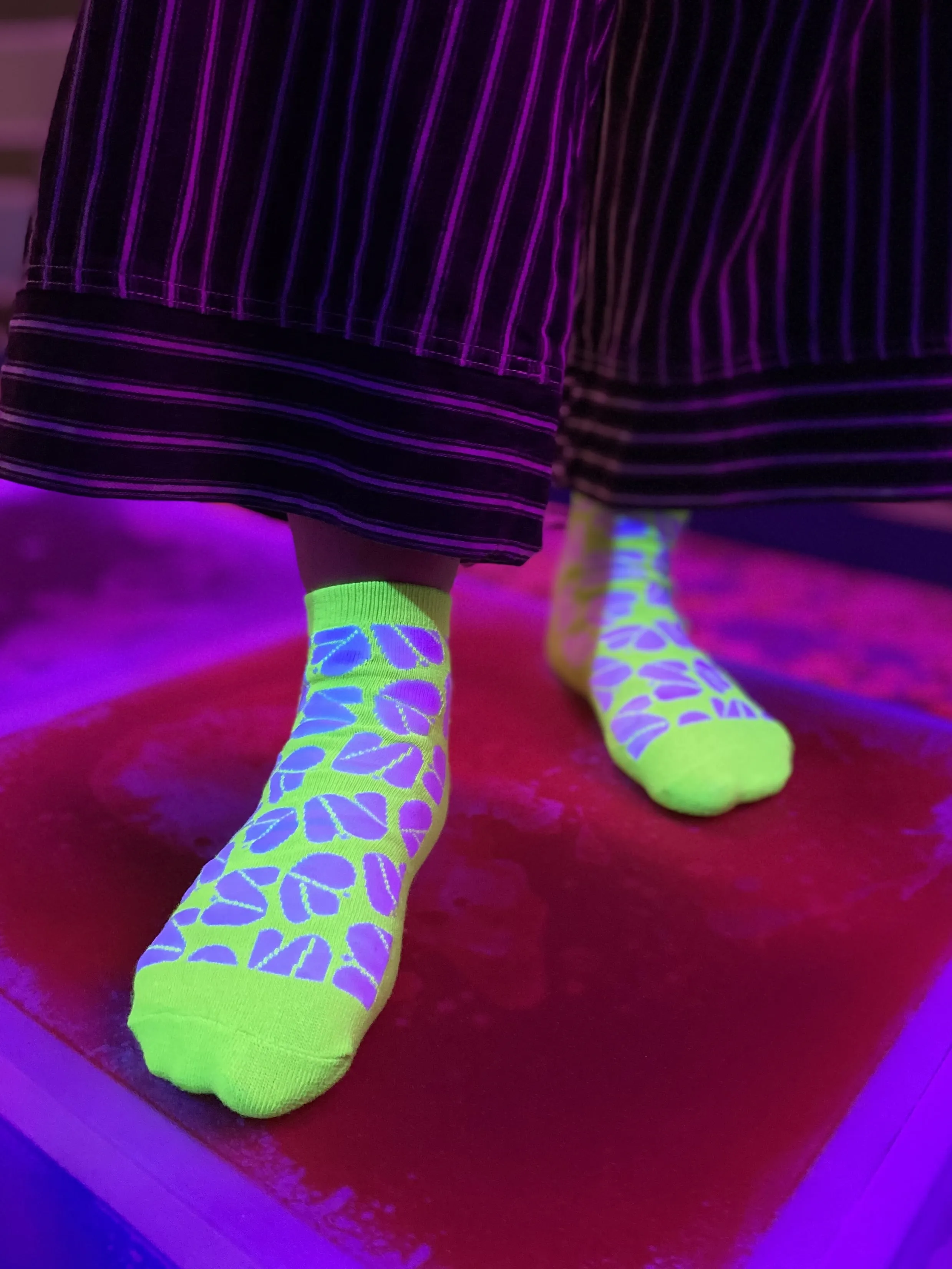 Persoon met neon-groene sokken met paarse patronen en zwart gestreepte broek onder UV-licht