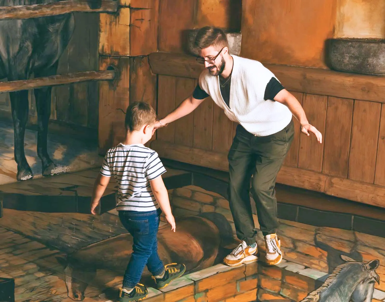 A man and a boy standing on a tilted floor illusion in a wooden room