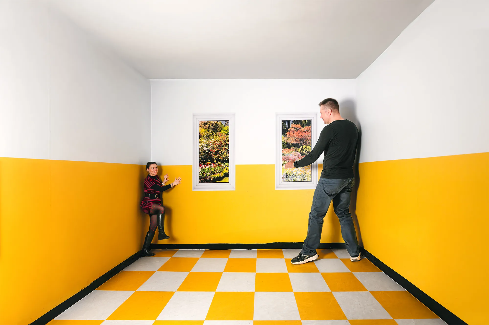 A man and a child in a room with yellow and white walls and a checkered floor, experiencing an optical illusion.
