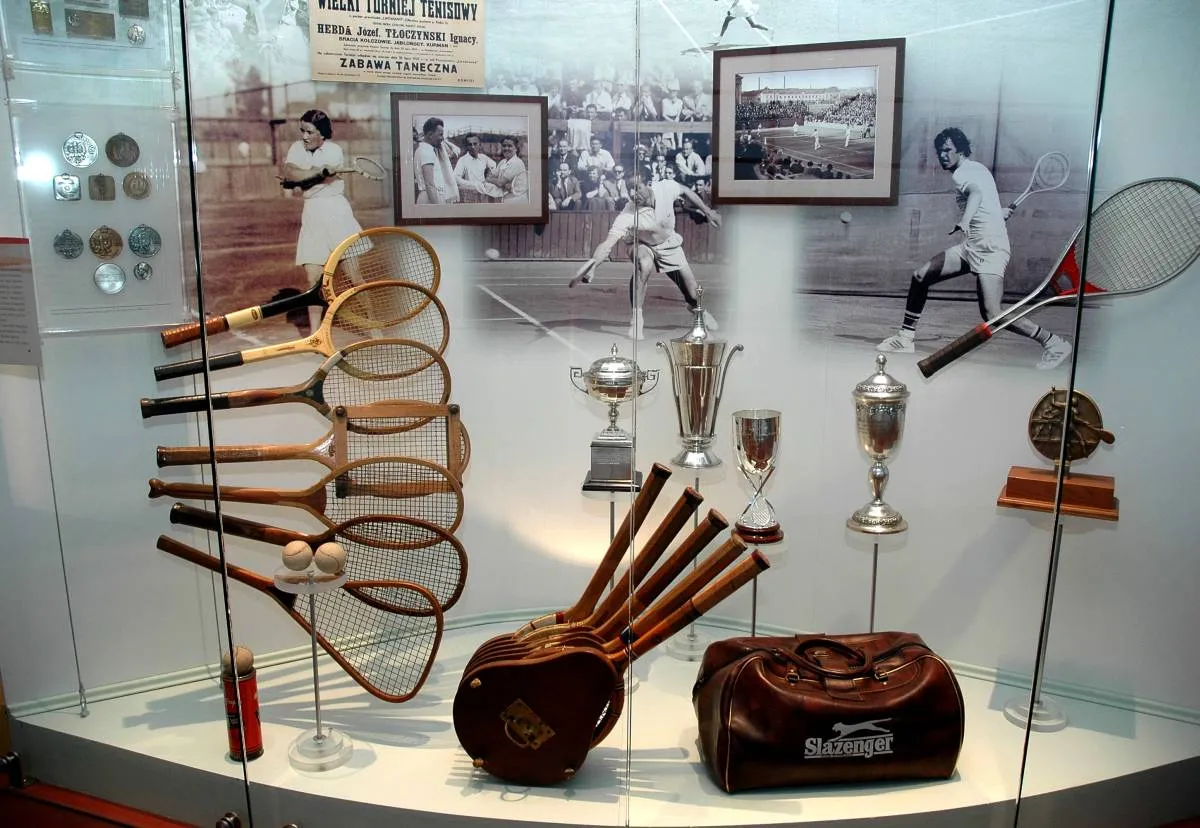 display case with vintage tennis rackets, trophies, and framed photographs in a museum exhibit