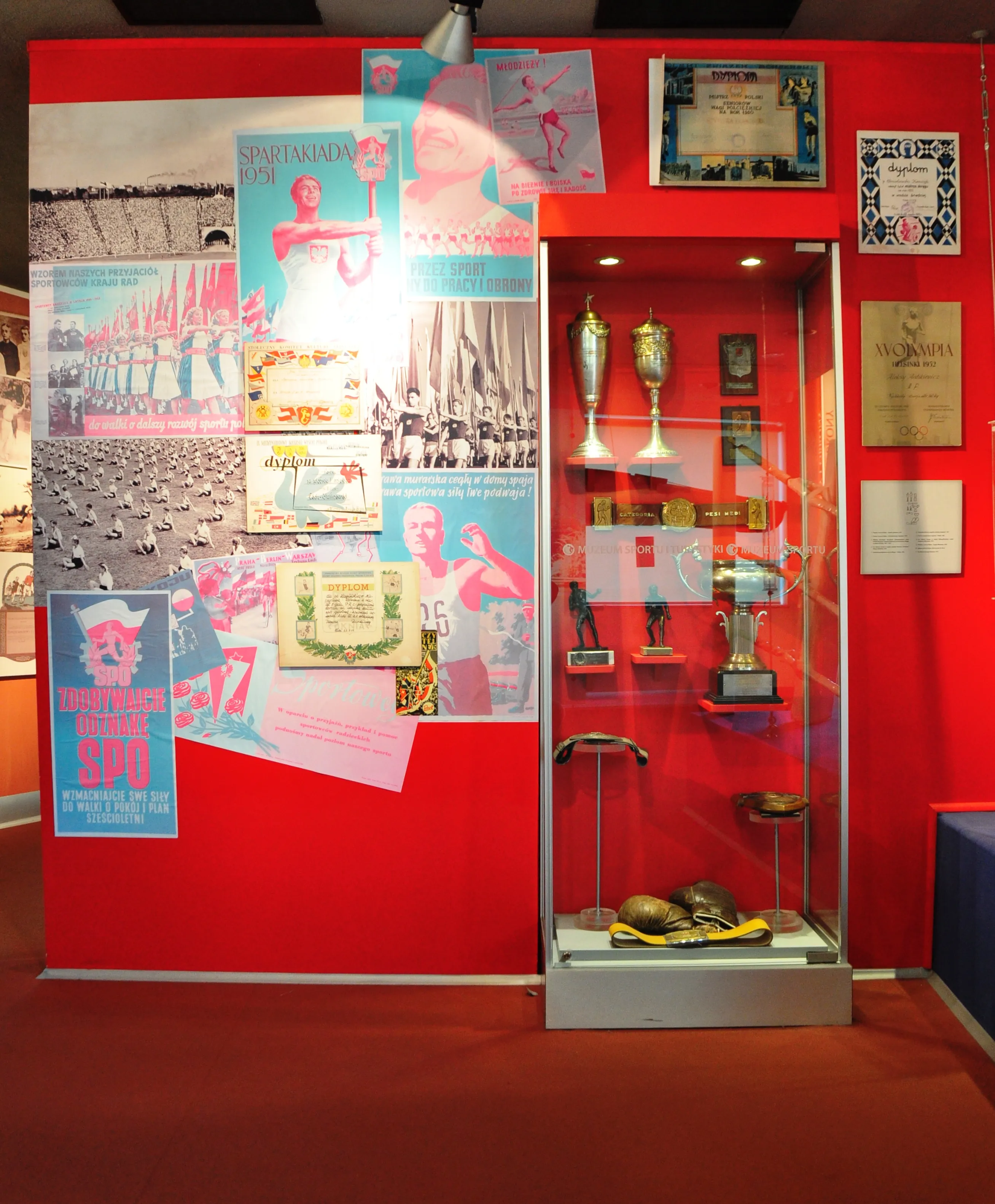 Red wall with posters and a glass display case with trophies and sports memorabilia