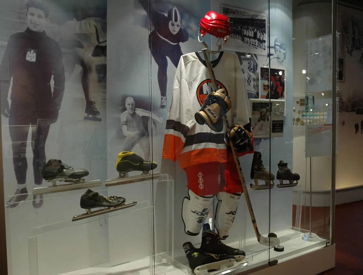 Hockey uniform and equipment on display in a glass case with athlete photos in the background