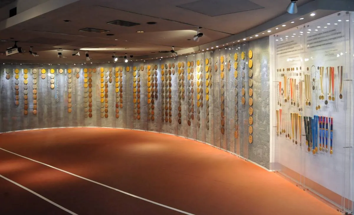 Curved wall display of medals in glass cases with a running track floor
