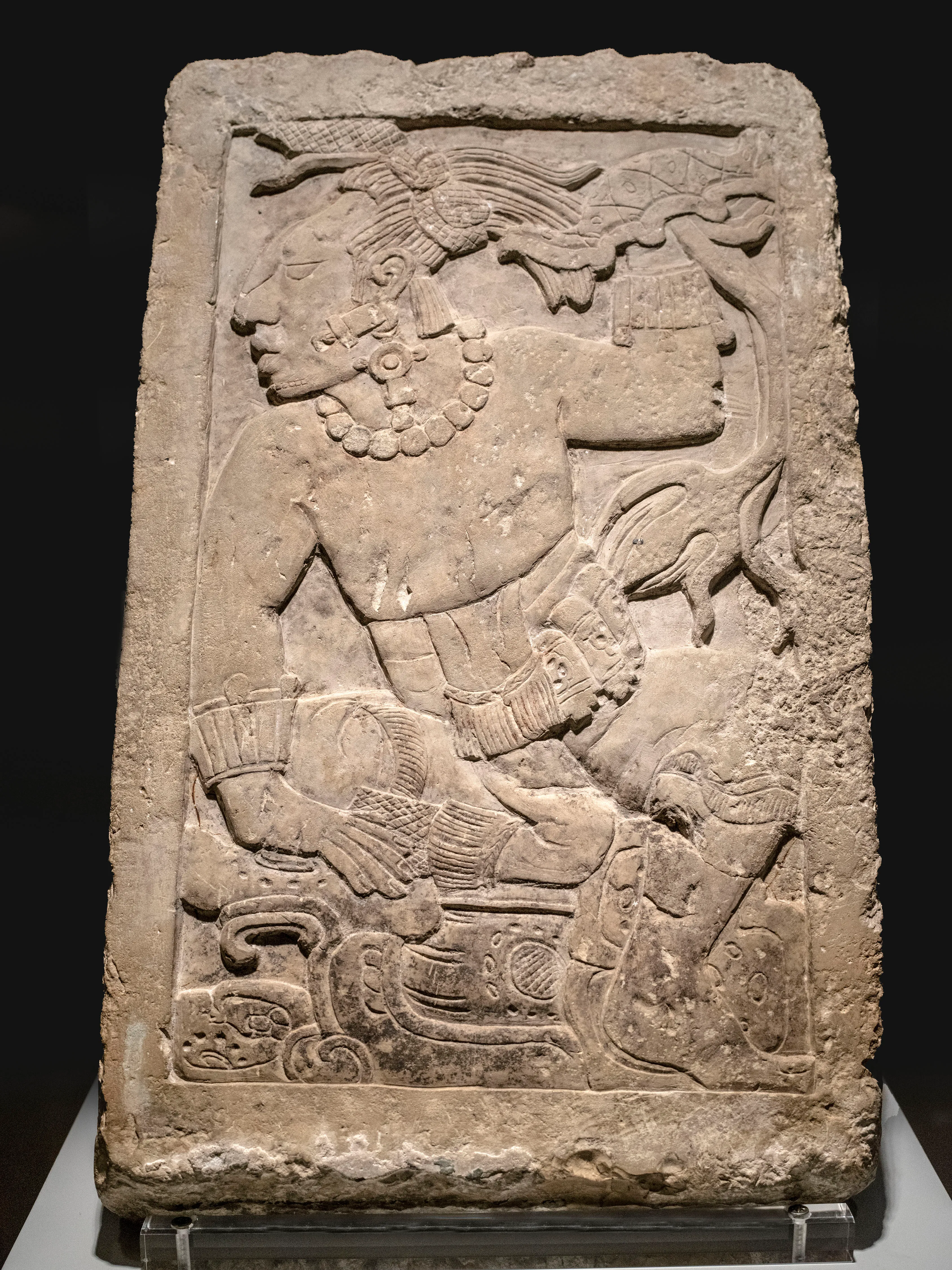 Gekerfde stenen stele met een figuur in traditionele kleding, tentoongesteld in een museum