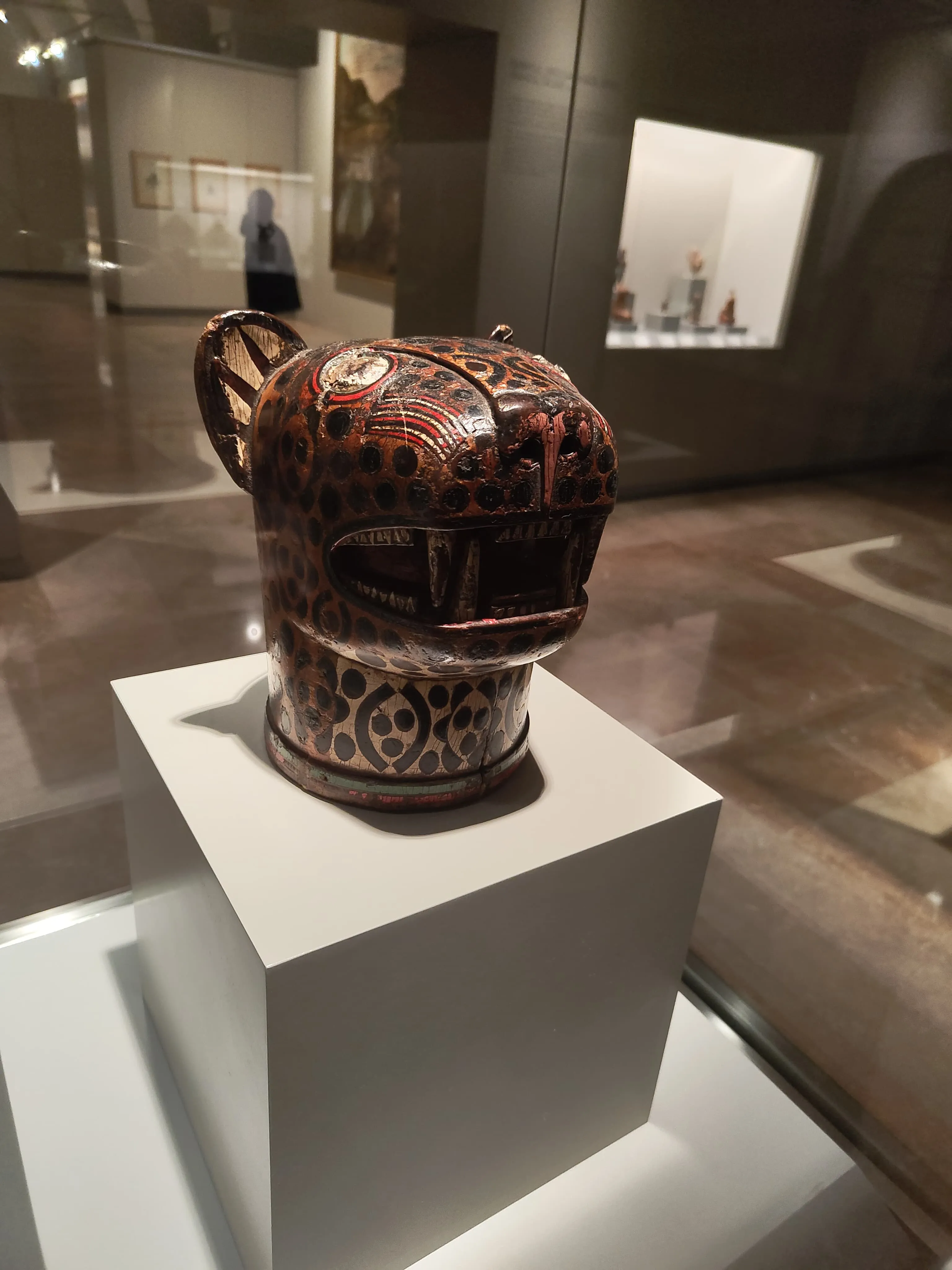 Een keramische jaguarvormige vaas met ingewikkelde beschilderde patronen, tentoongesteld op een wit voetstuk in een museumgalerij