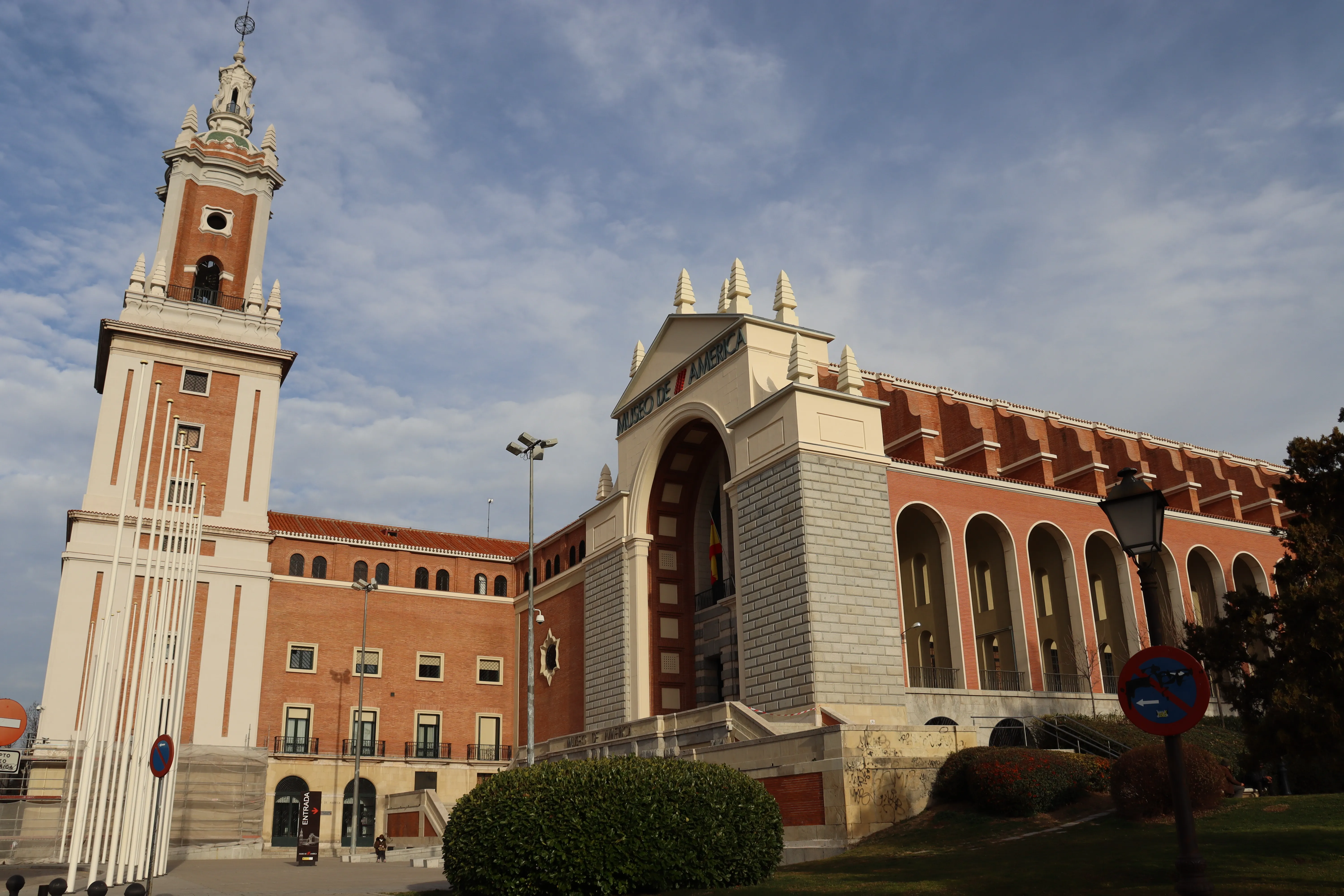Zewnętrzna część Muzeum Ameryk z wysoką wieżą zegarową i łukowym wejściem pod częściowo zachmurzonym niebem