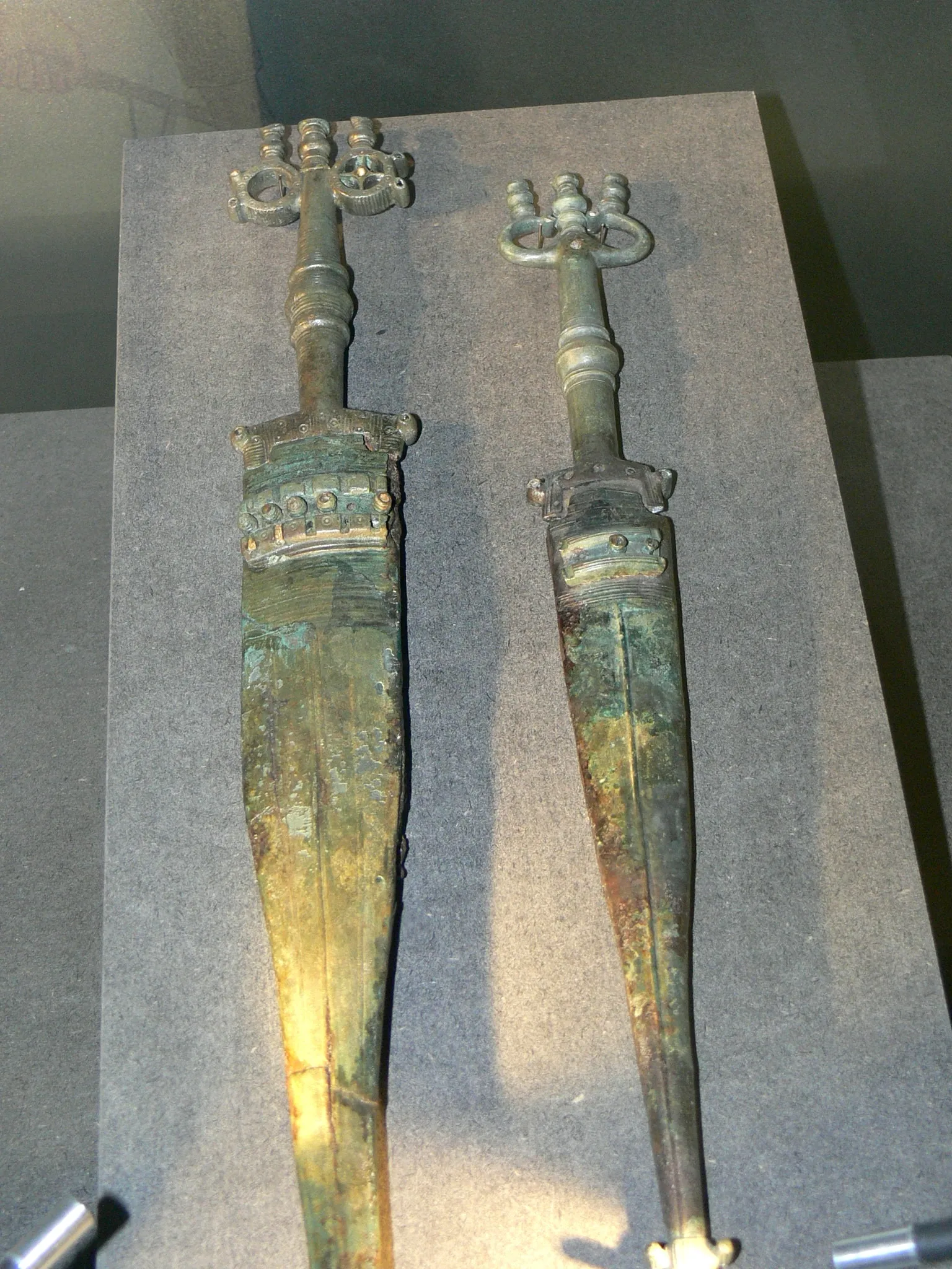 Two ancient Celtic bronze swords with ornate ring-decorated hilts displayed side by side on a gray museum surface
