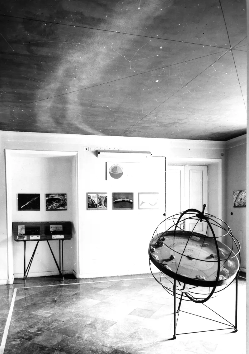 Interior de una galería de museo con una esfera armilar, expositores enmarcados y un techo estampado