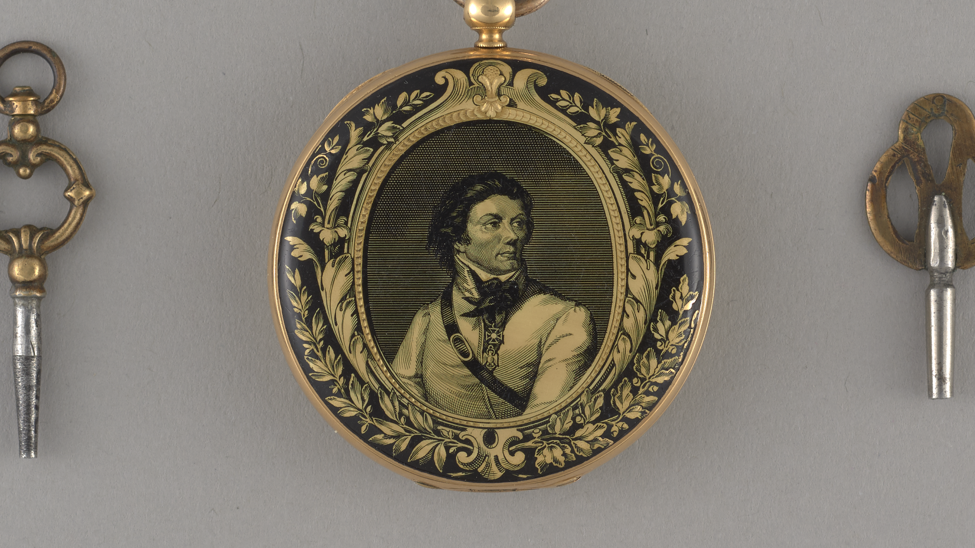 Een zakhorloge met een portret van een man in een gouden lijst en twee sleutels op een grijze ondergrond