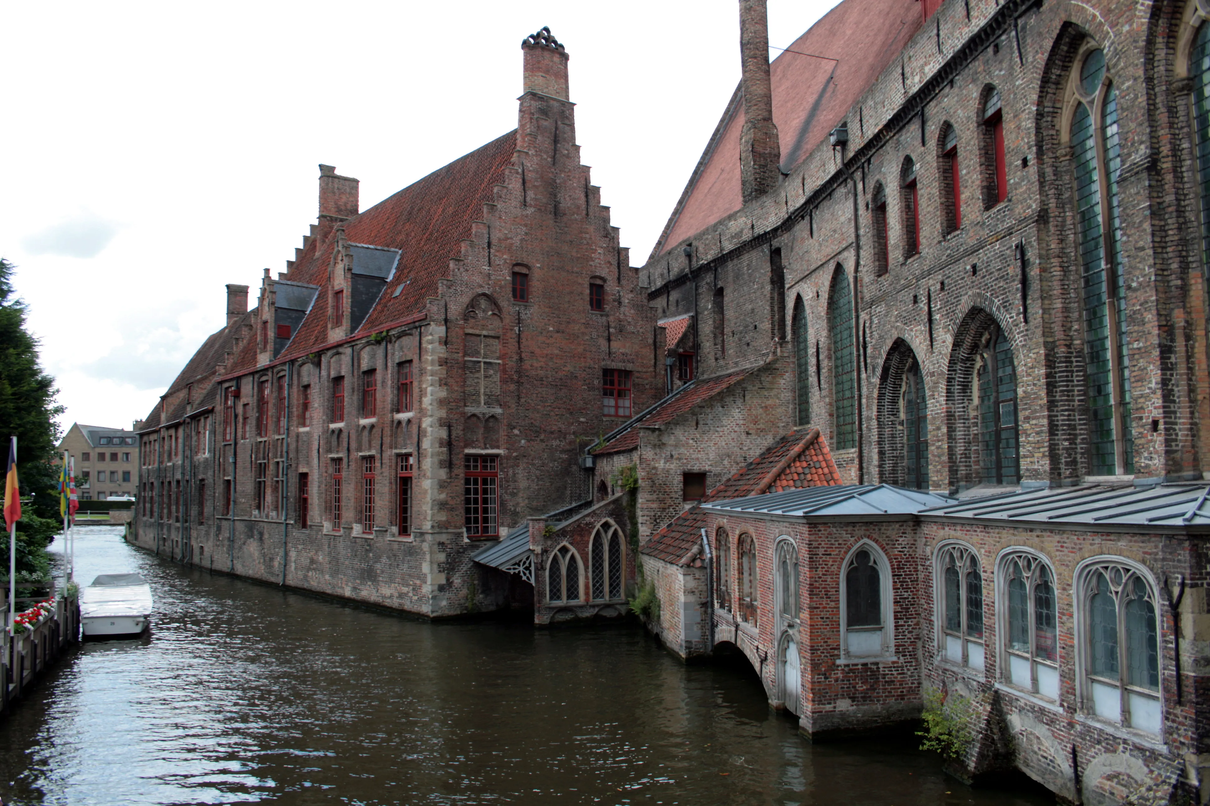 Historic brick hospital complex with Gothic arched windows and stepped gables along a canal in Bruges