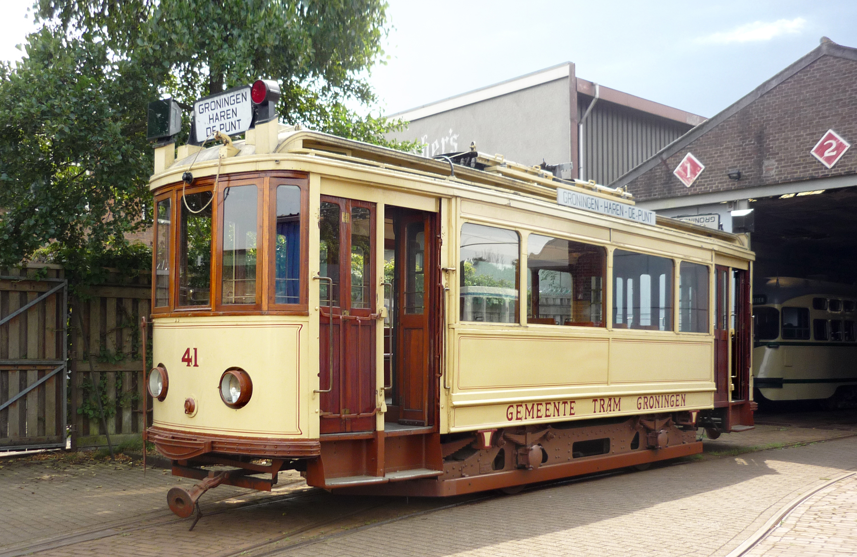 A vintage tram with cream and brown panels, numbered 41, parked outdoors near a building with overhead wires.