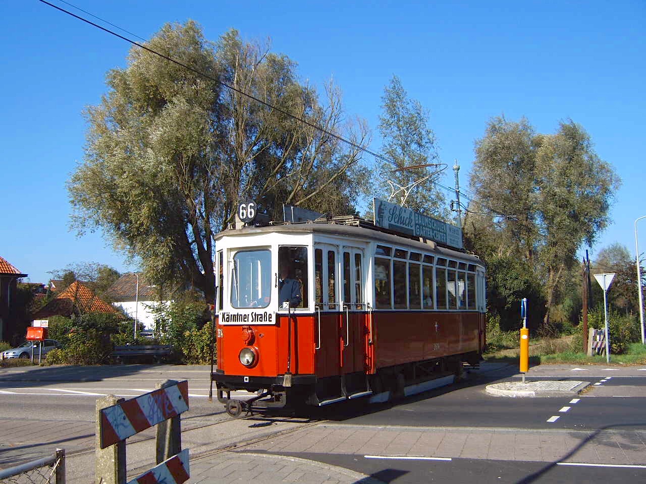 Czerwony i biały zabytkowy tramwaj z numerem 66 na ulicy pod błękitnym niebem