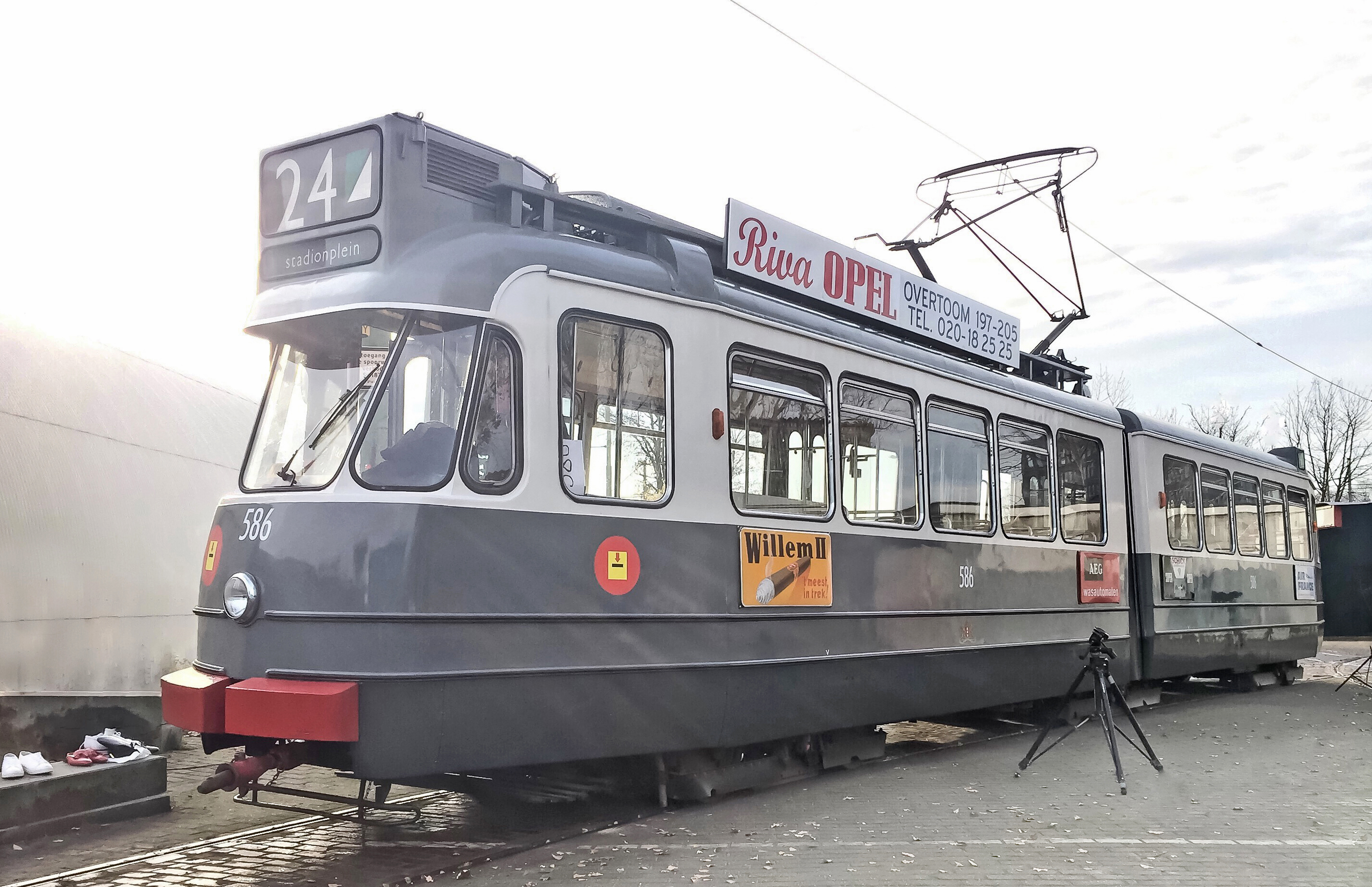A gray and red vintage tram with the number 24 on its destination sign and an advertisement for 'Riva OP!' on its side