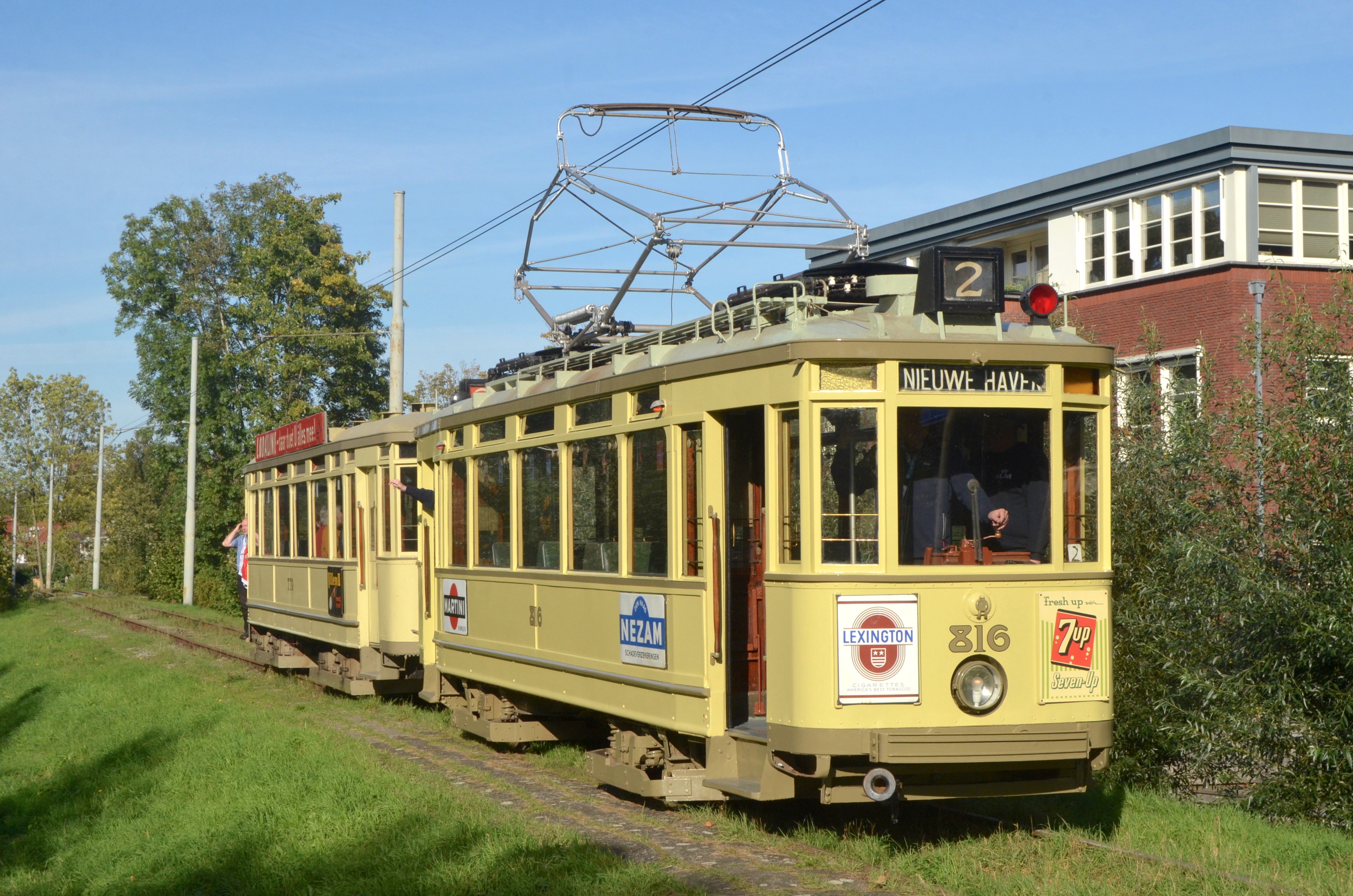 Żółty zabytkowy tramwaj na torach z przewodami napowietrznymi i budynkiem w tle